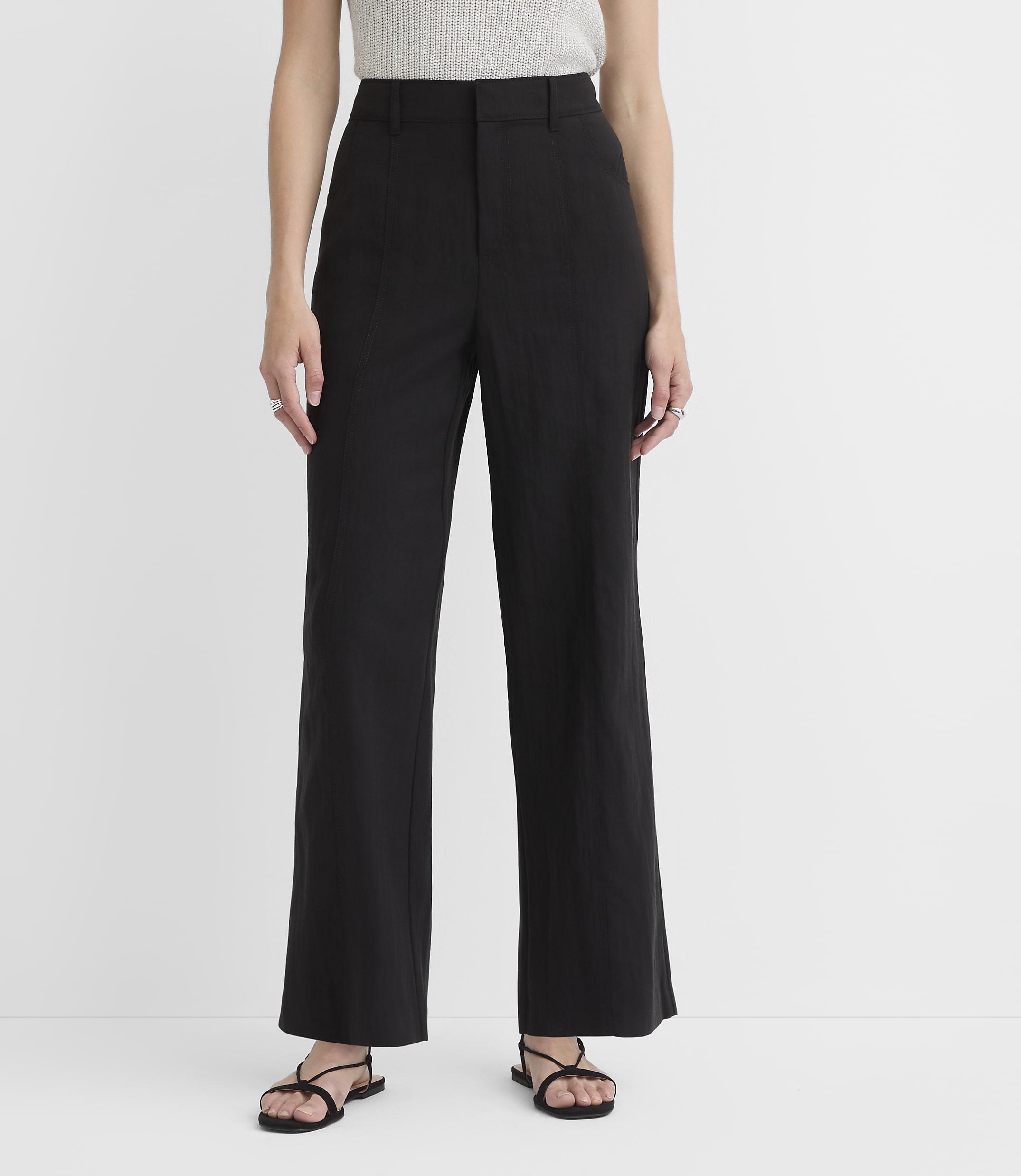 A person stands in black wide-leg pants and sandals against a plain white background.