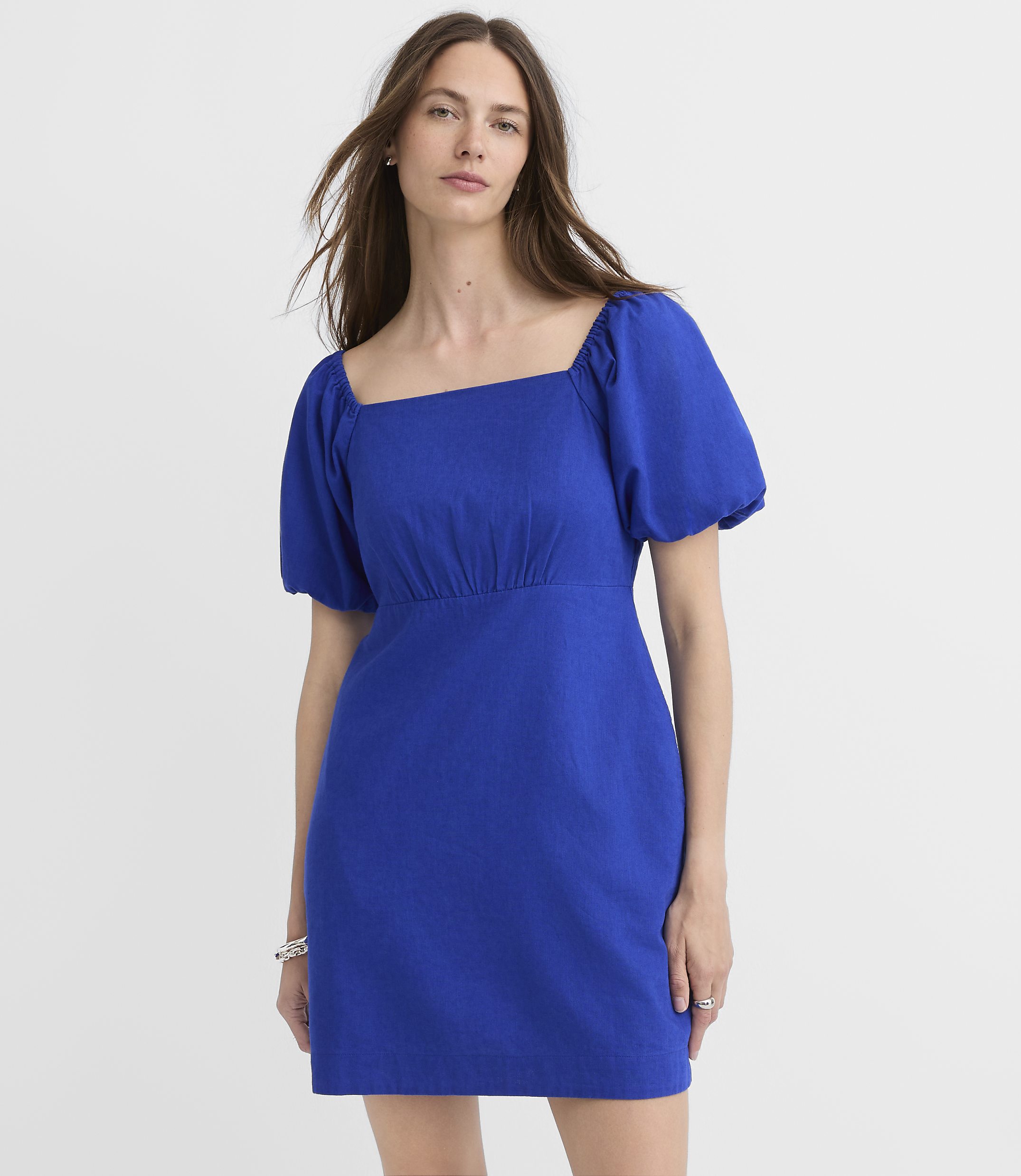 A woman in a blue puff-sleeve dress stands against a plain white background.