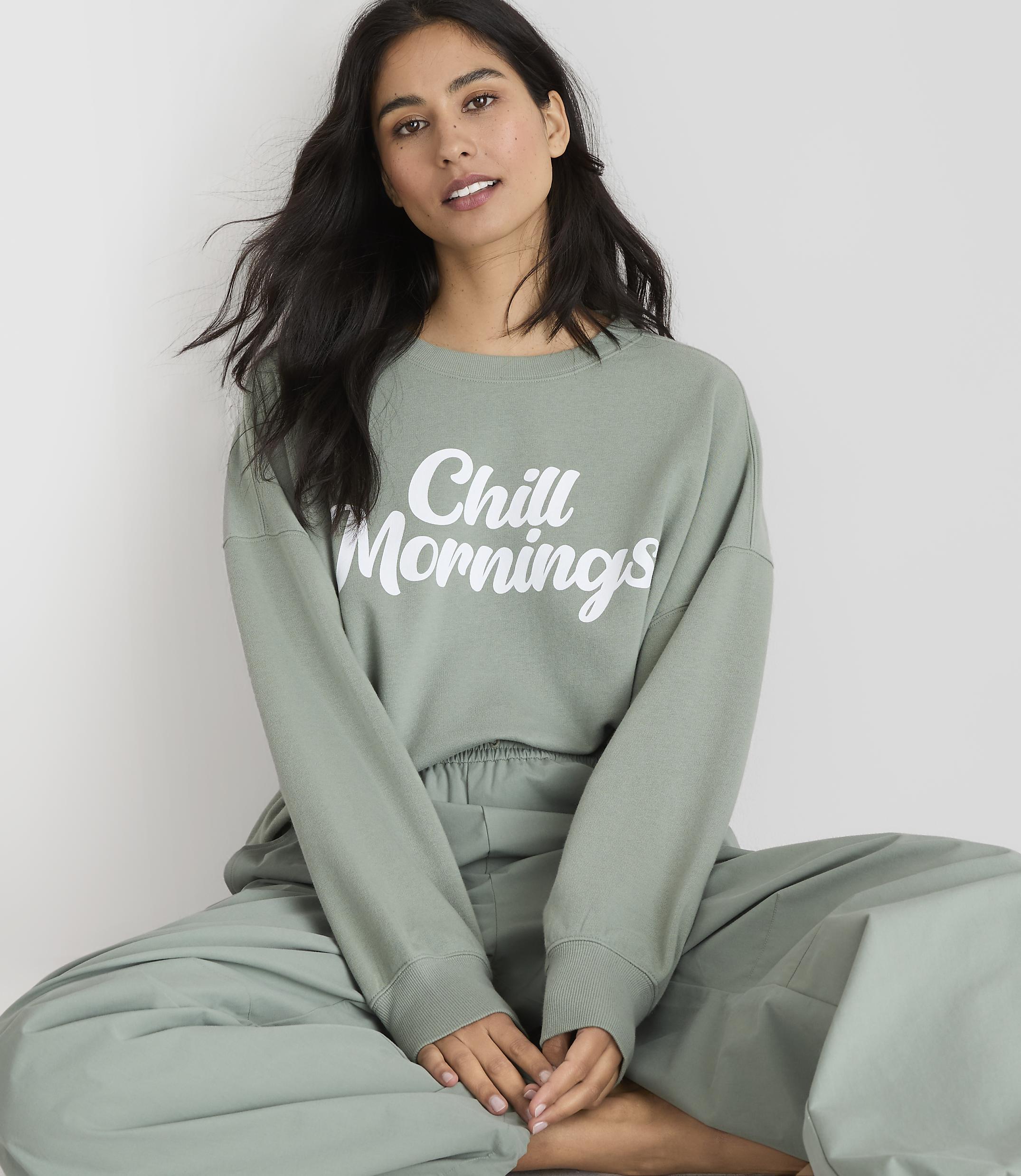 A woman in a green sweatshirt and pants sits against a plain white background.