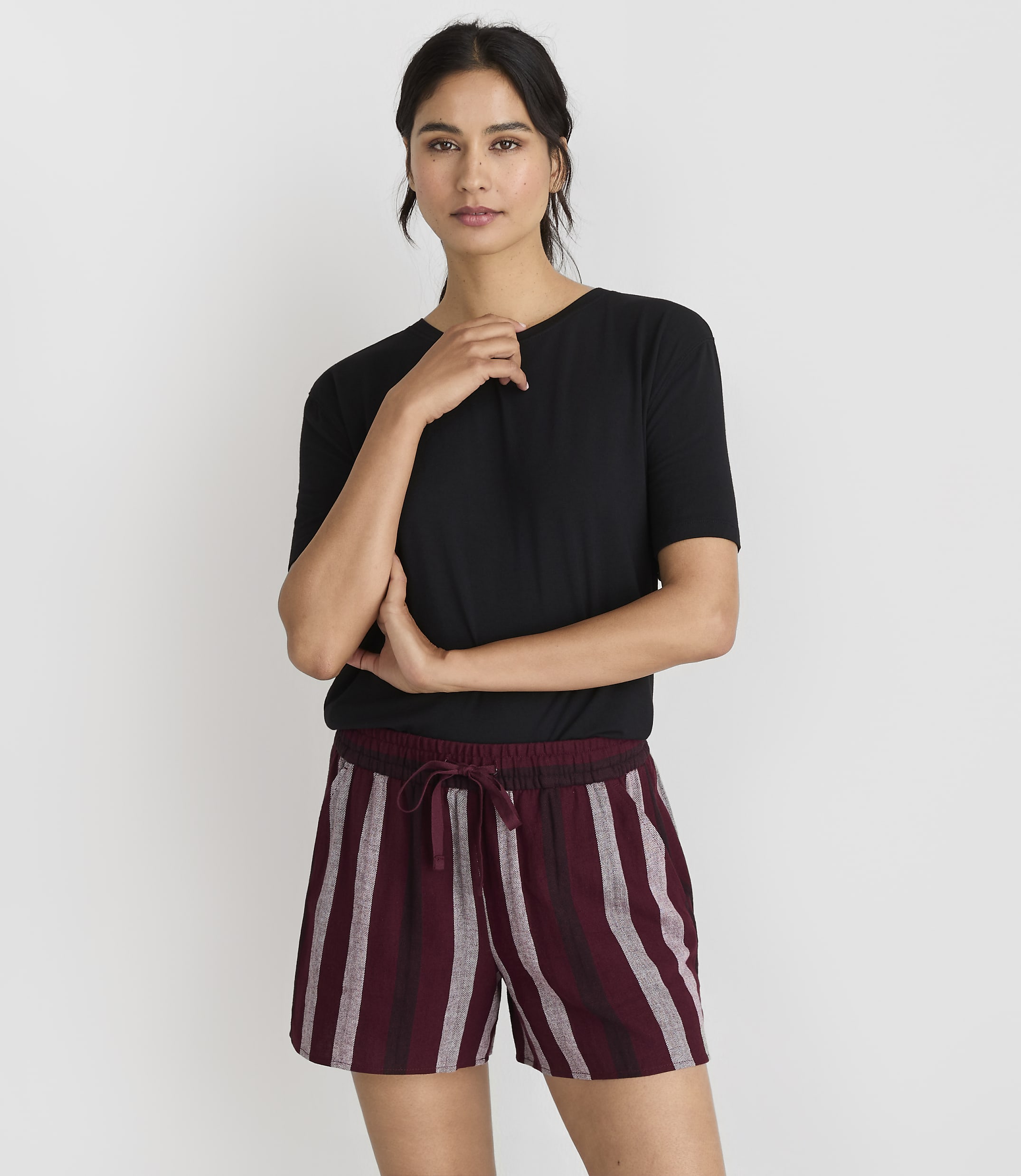 A woman in a black t-shirt and striped shorts stands against a plain white background.