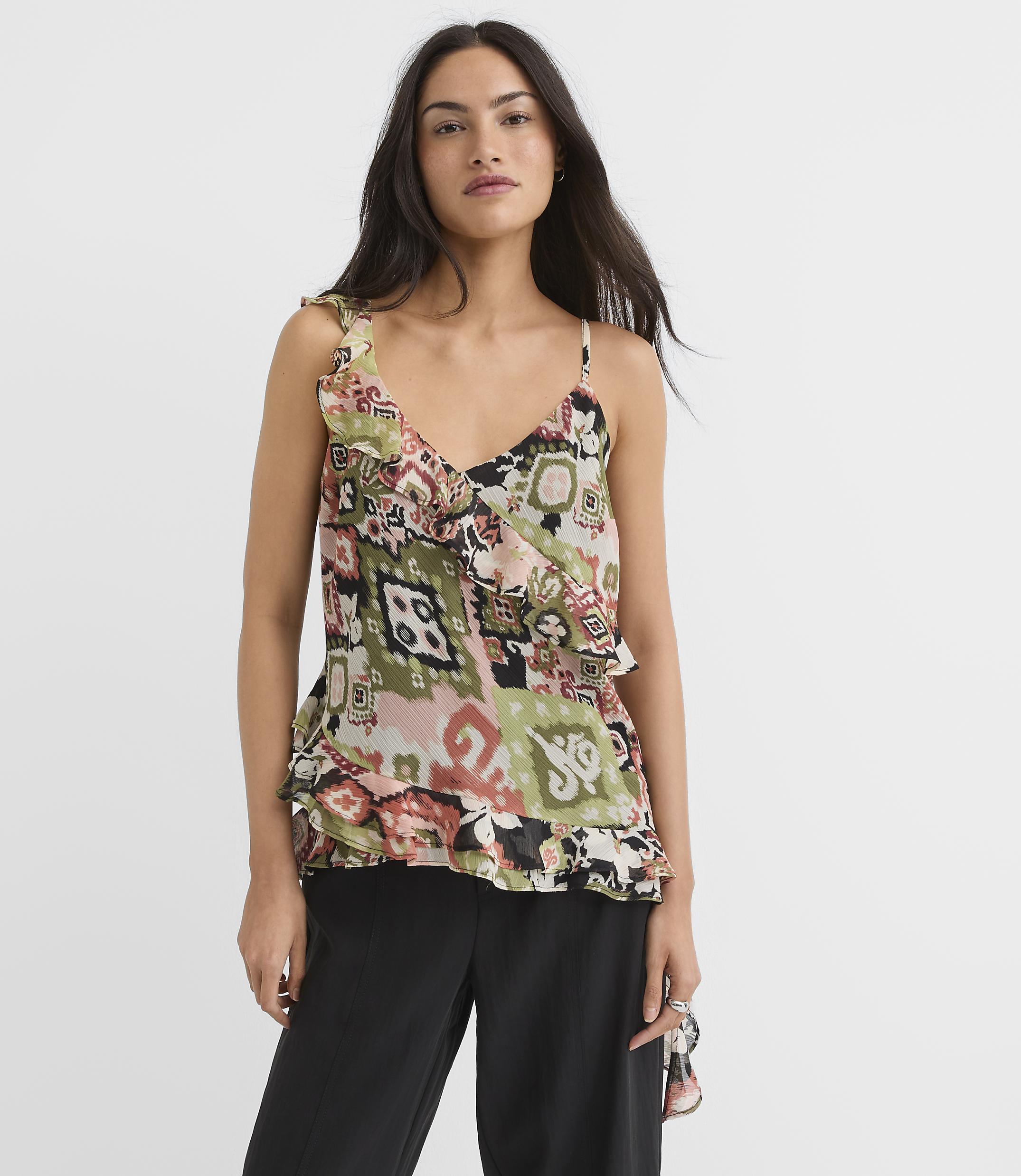 A woman in a patterned camisole and black pants stands against a plain white background.