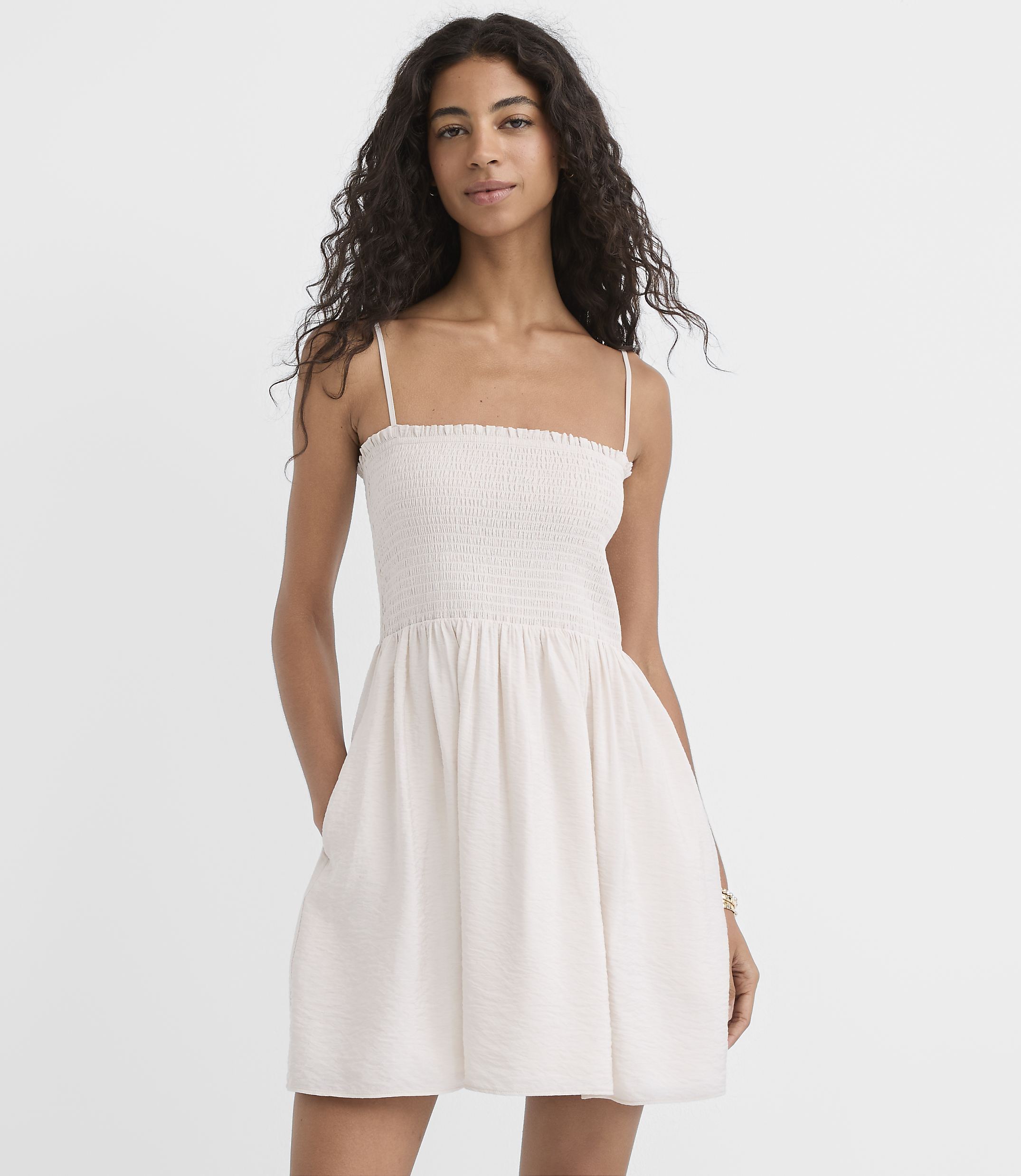A woman in a white smocked dress stands against a plain white background.