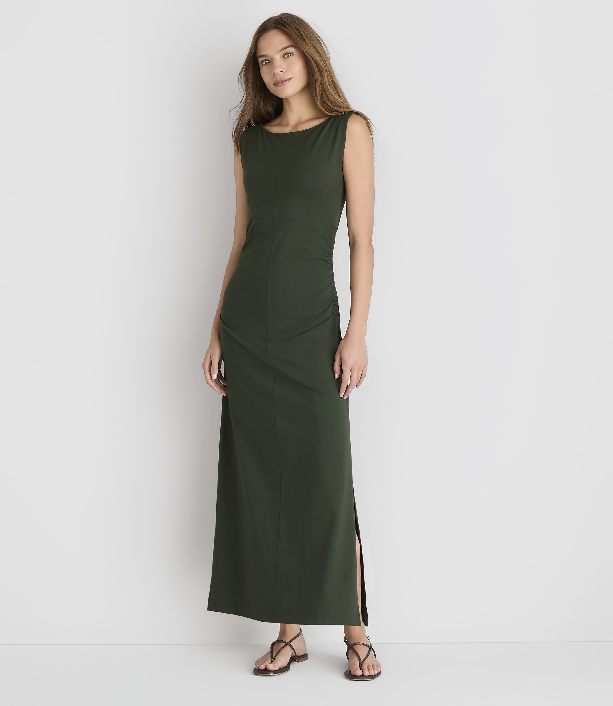 A woman in a dark green maxi dress stands against a plain white background.