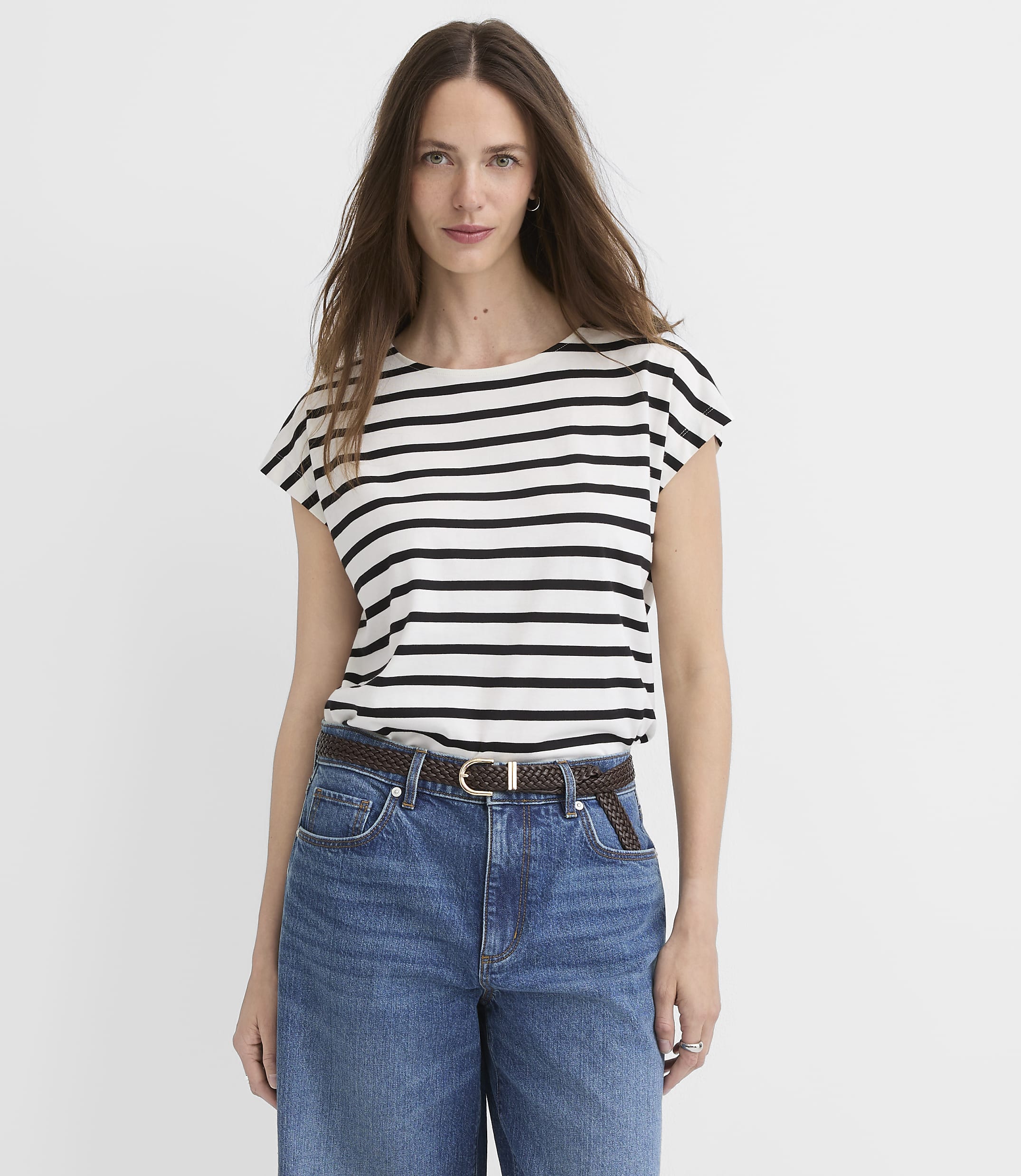 A woman in a striped shirt and jeans stands against a plain white background.