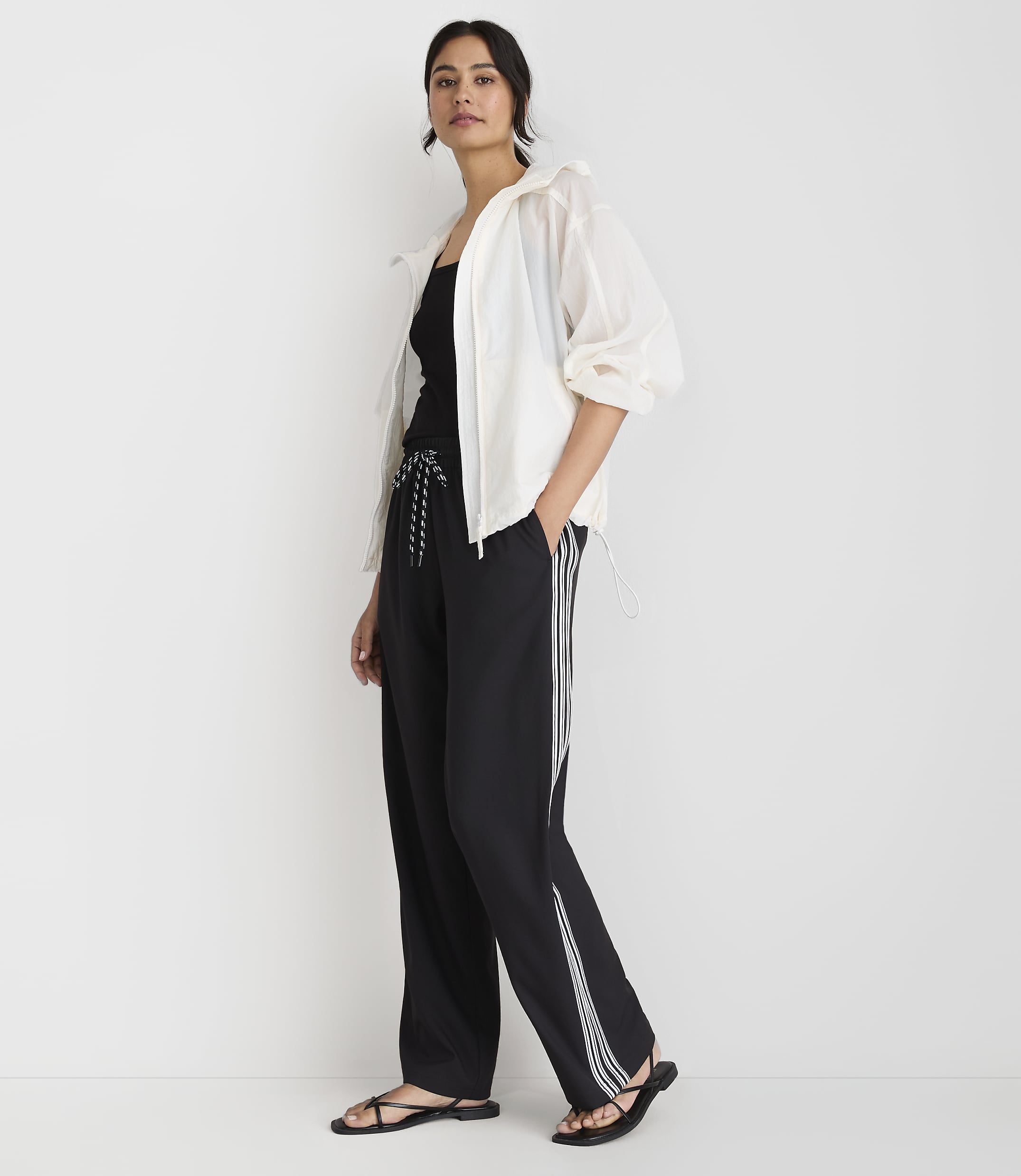 A woman in a white jacket and black athletic pants stands against a plain white background.