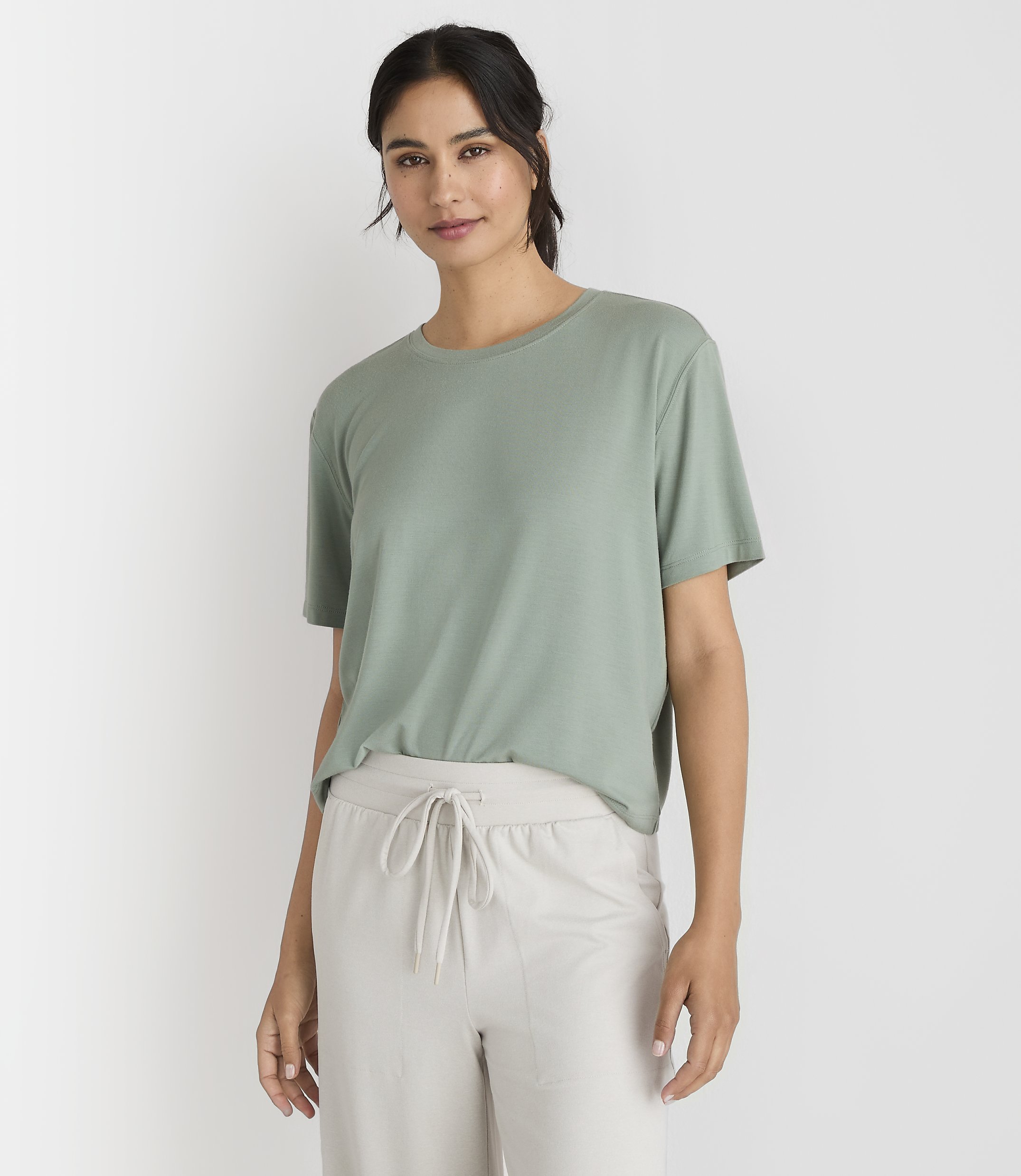 A woman in a green t-shirt and light-colored pants stands against a plain white background.