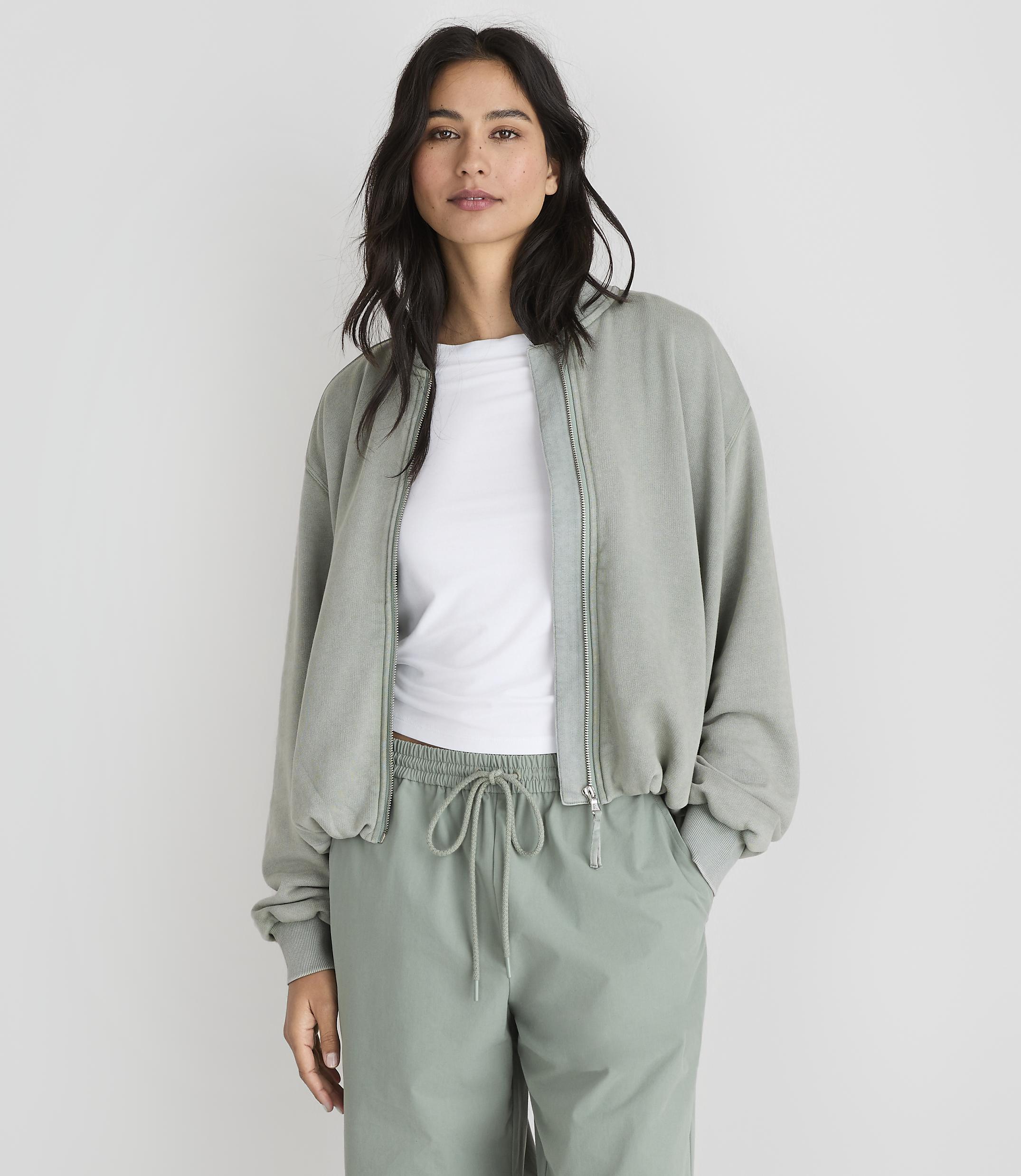 A woman in a light green bomber jacket and matching pants stands against a plain white background.