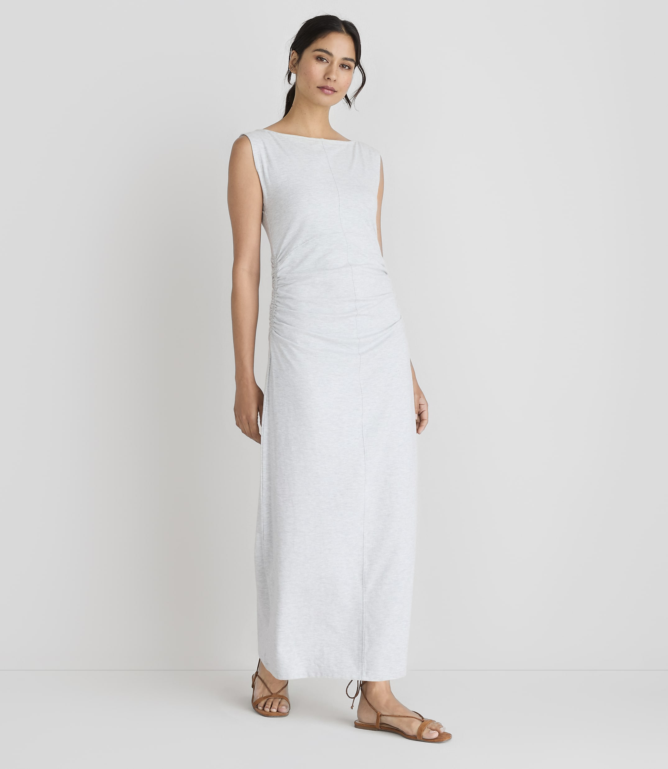 A woman in a light-colored, ruched maxi dress stands against a plain white background.