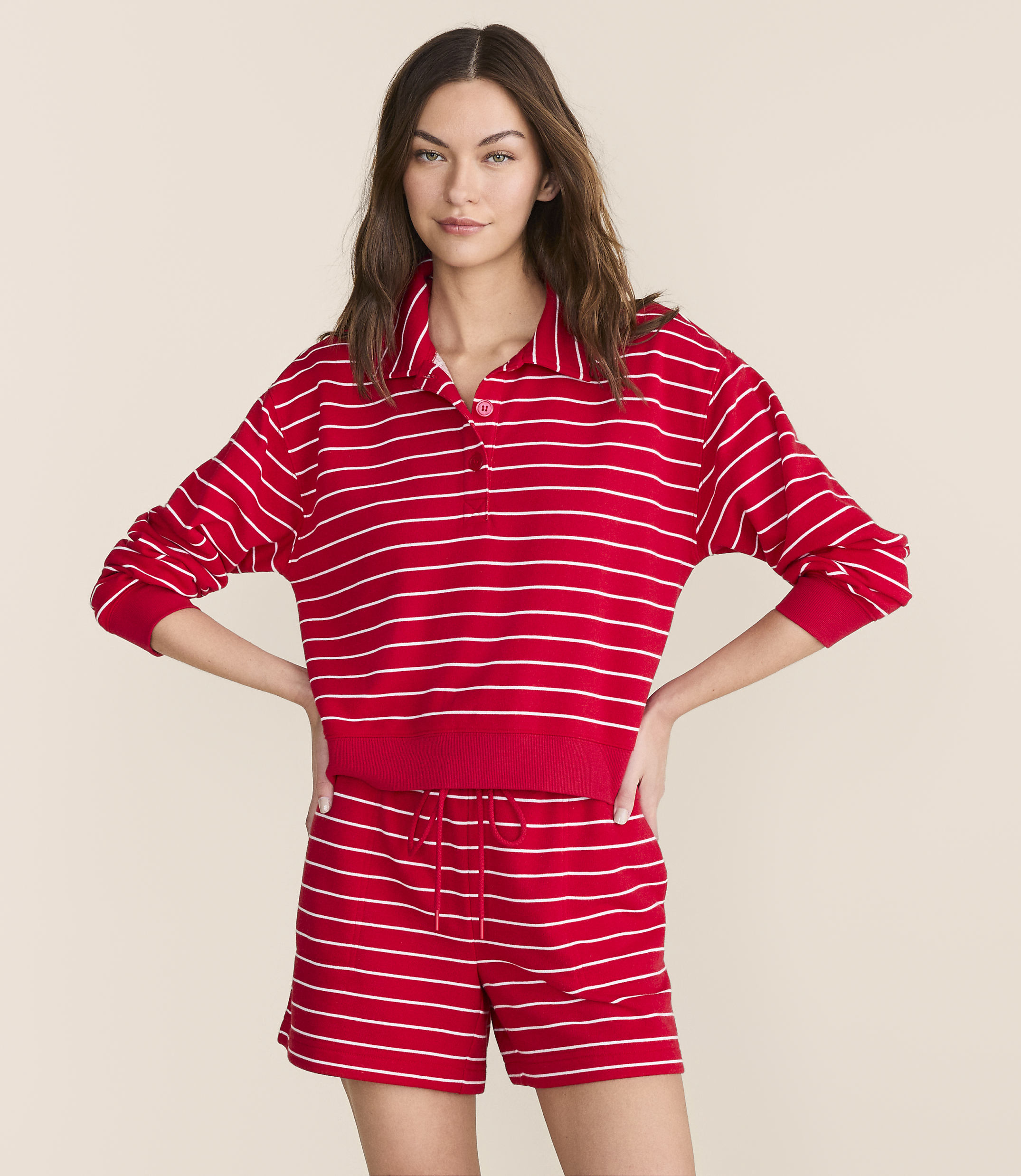 A woman in a red and white striped polo shirt and matching shorts stands against a plain, light-colored background.