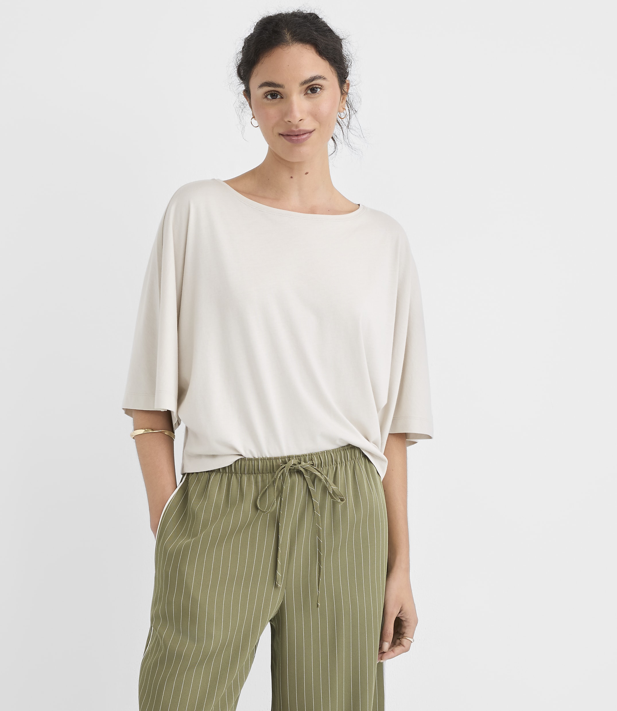 A woman in a light-colored oversized shirt and green striped pants stands against a plain white background.