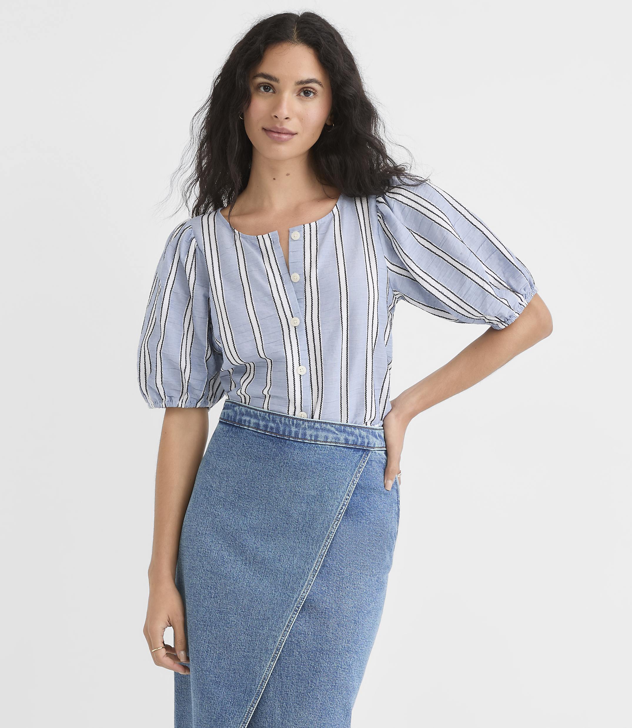 A woman in a striped puff-sleeve blouse and a denim skirt stands against a plain white background.