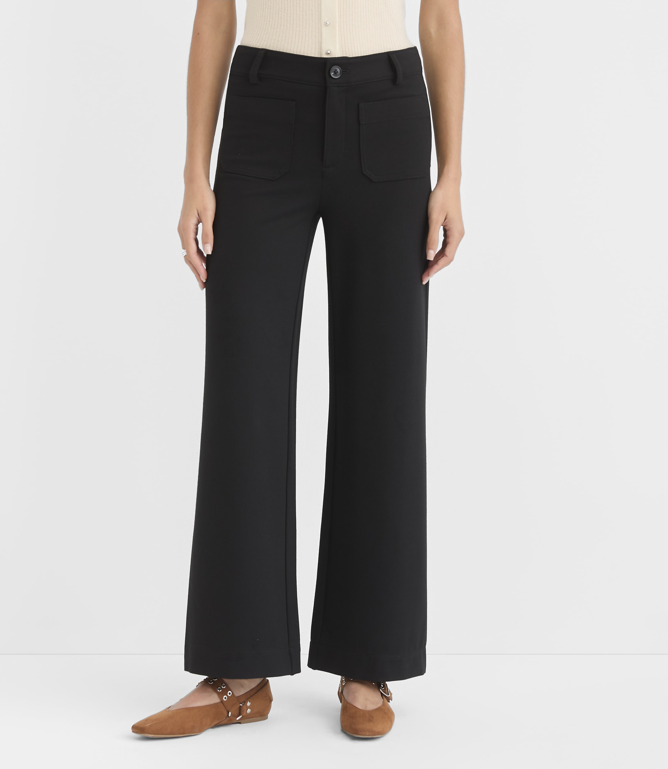 A person stands in black wide-leg pants and brown flats against a plain white background.