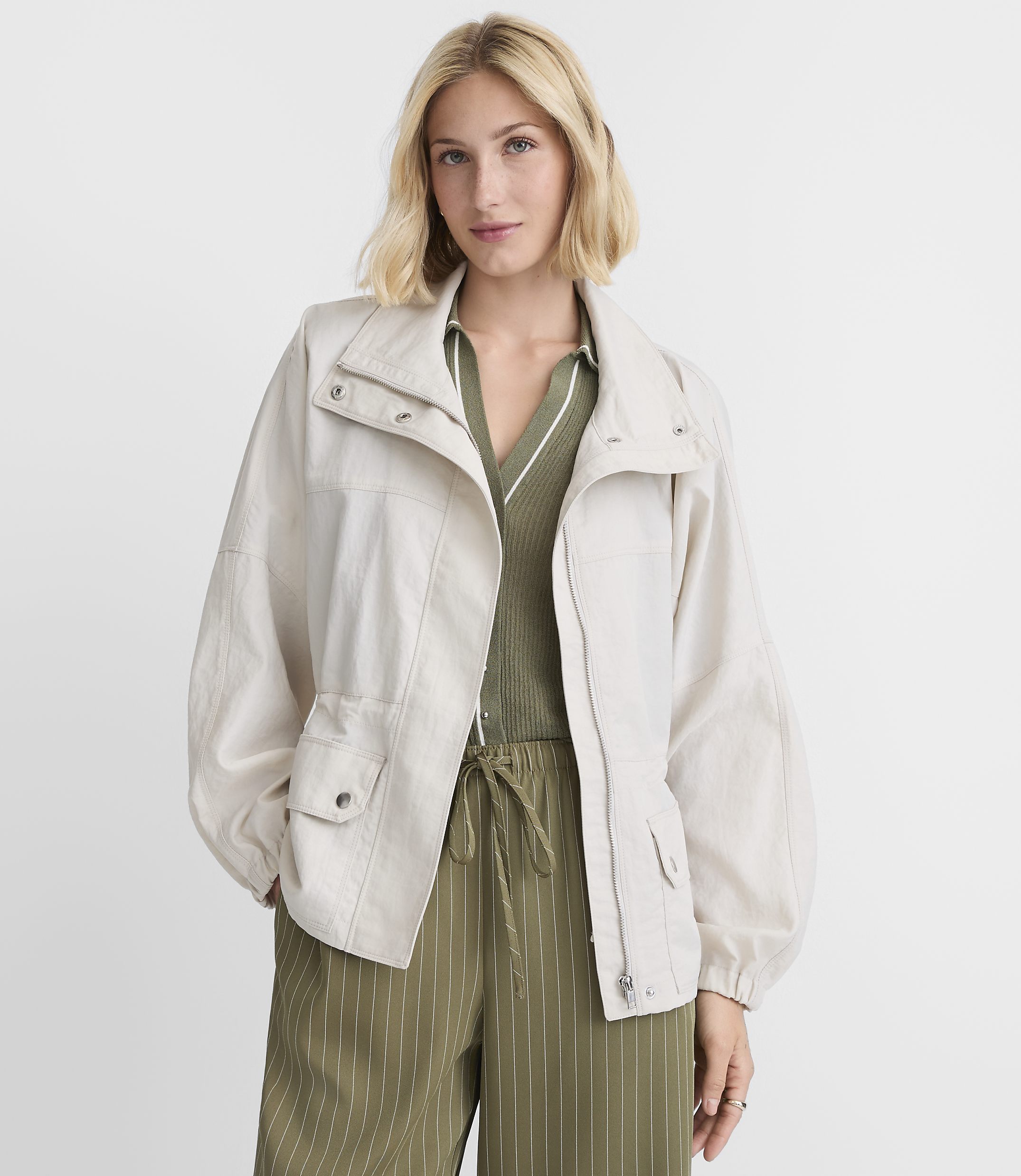 A woman in a light-colored jacket and green striped pants stands against a plain white background.