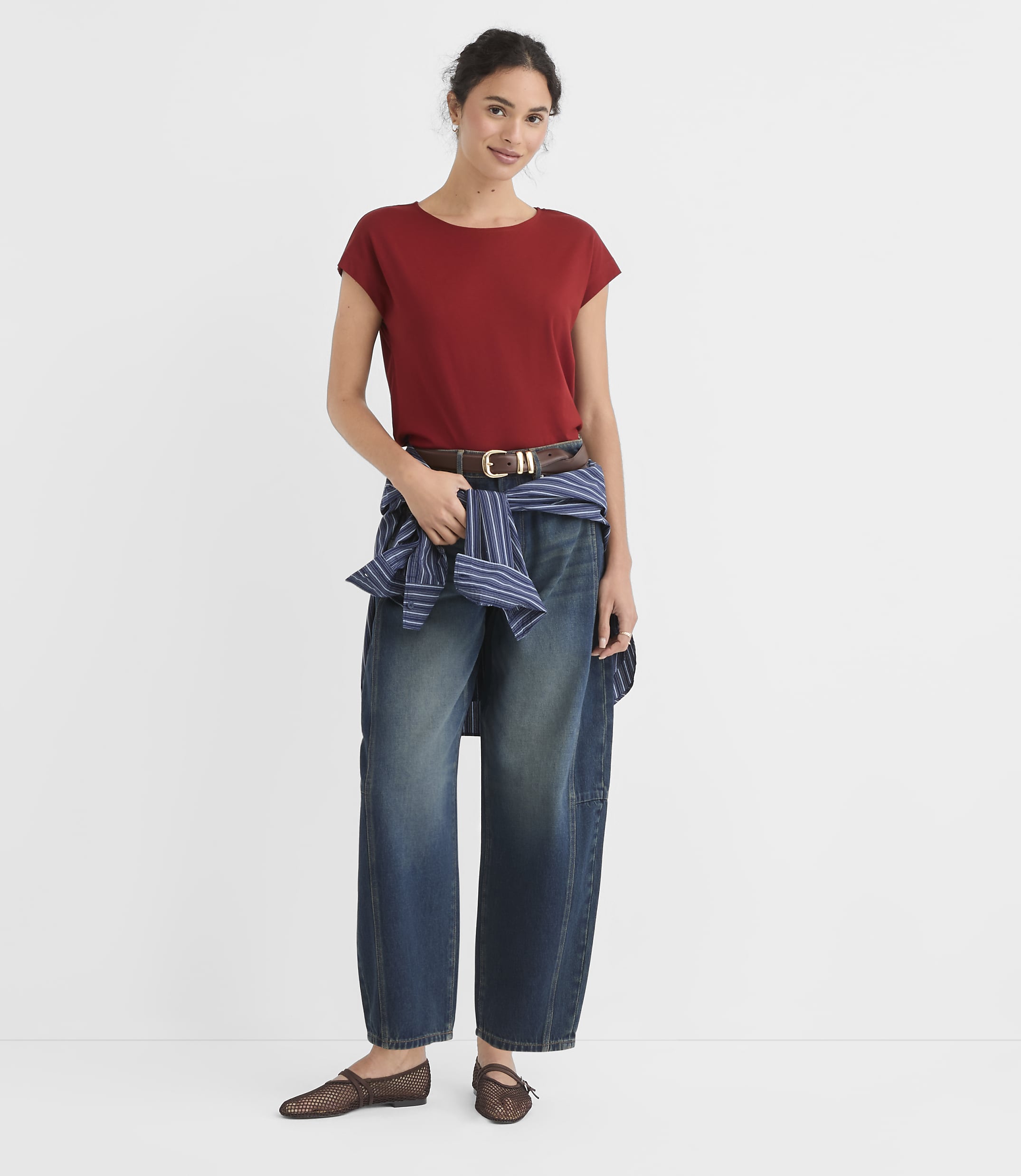 A woman in a red t-shirt and wide-leg jeans stands against a plain white background.