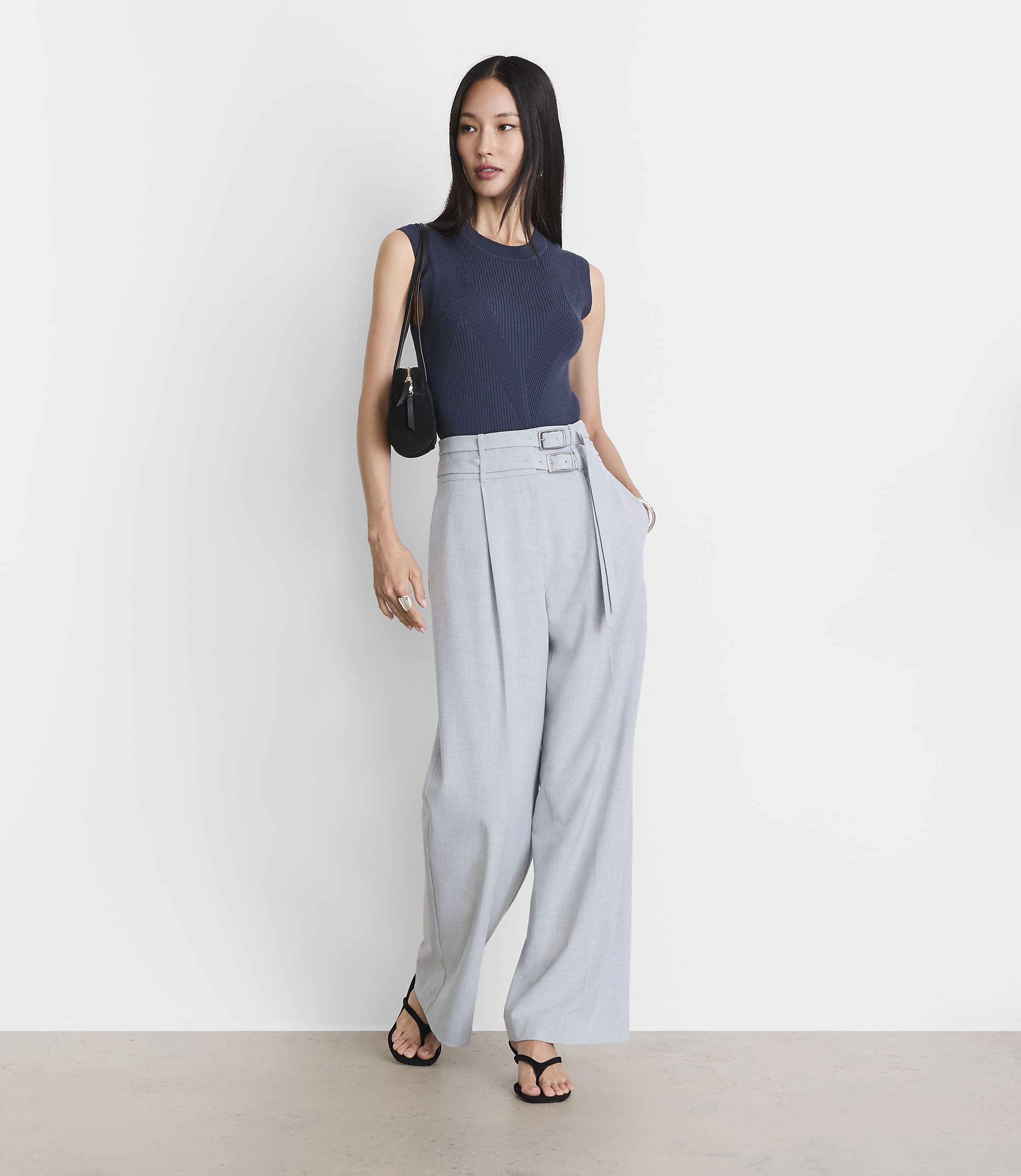A woman in a navy top and light gray wide-leg pants stands against a plain white background.