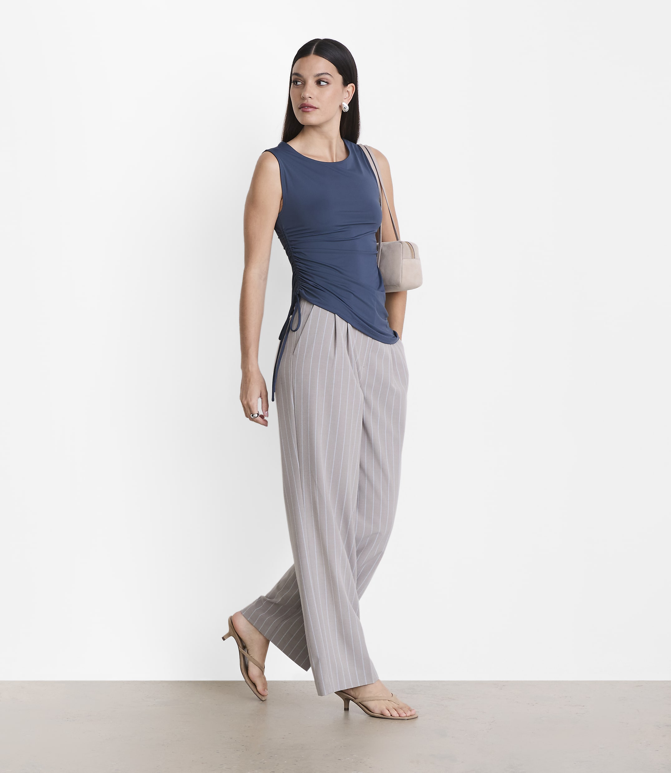 A woman in a blue top and striped pants stands against a plain white background.