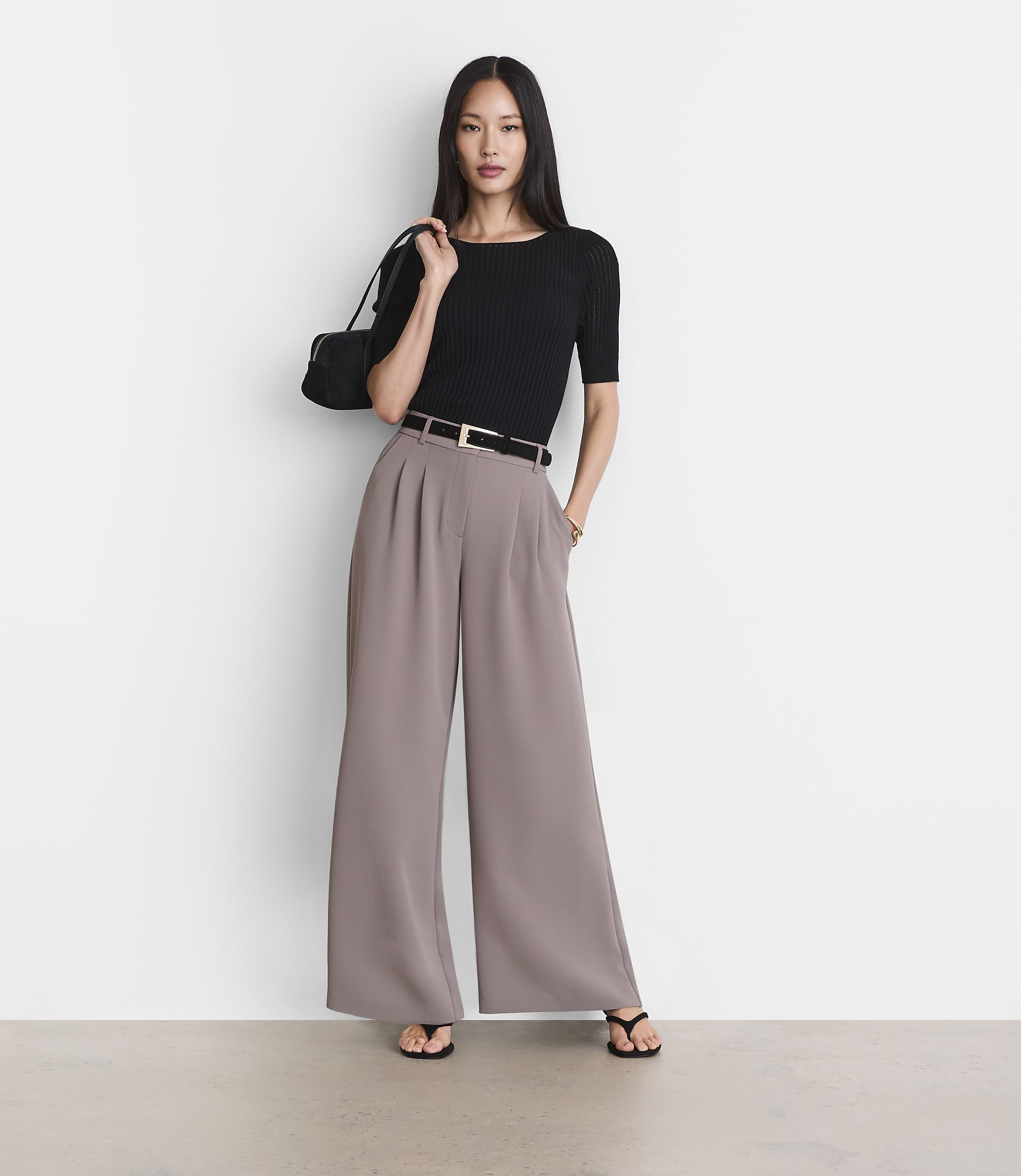 A woman in a black top and wide-leg pants stands against a plain white background.
