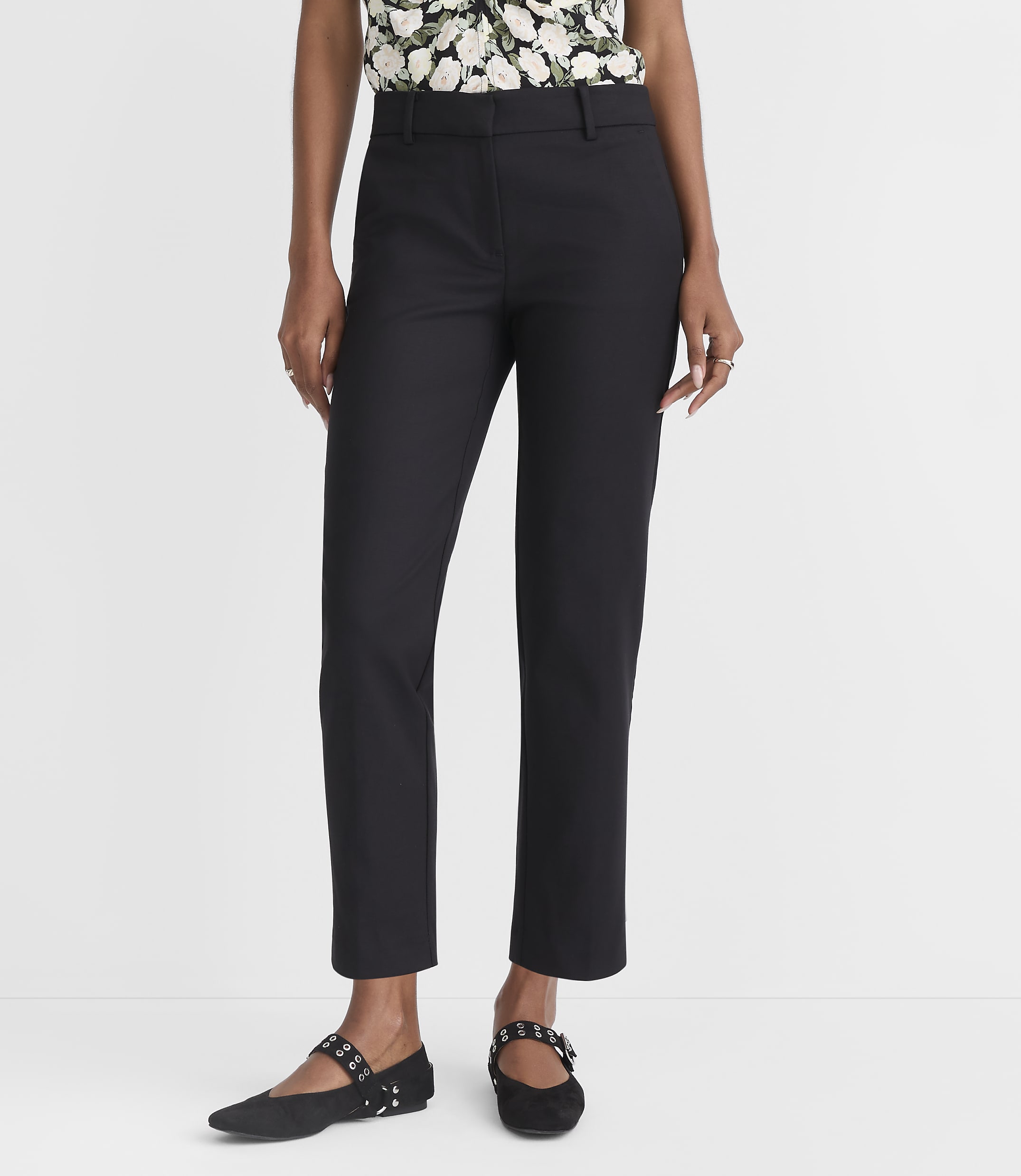 A person in black pants and a floral top stands against a plain white background.