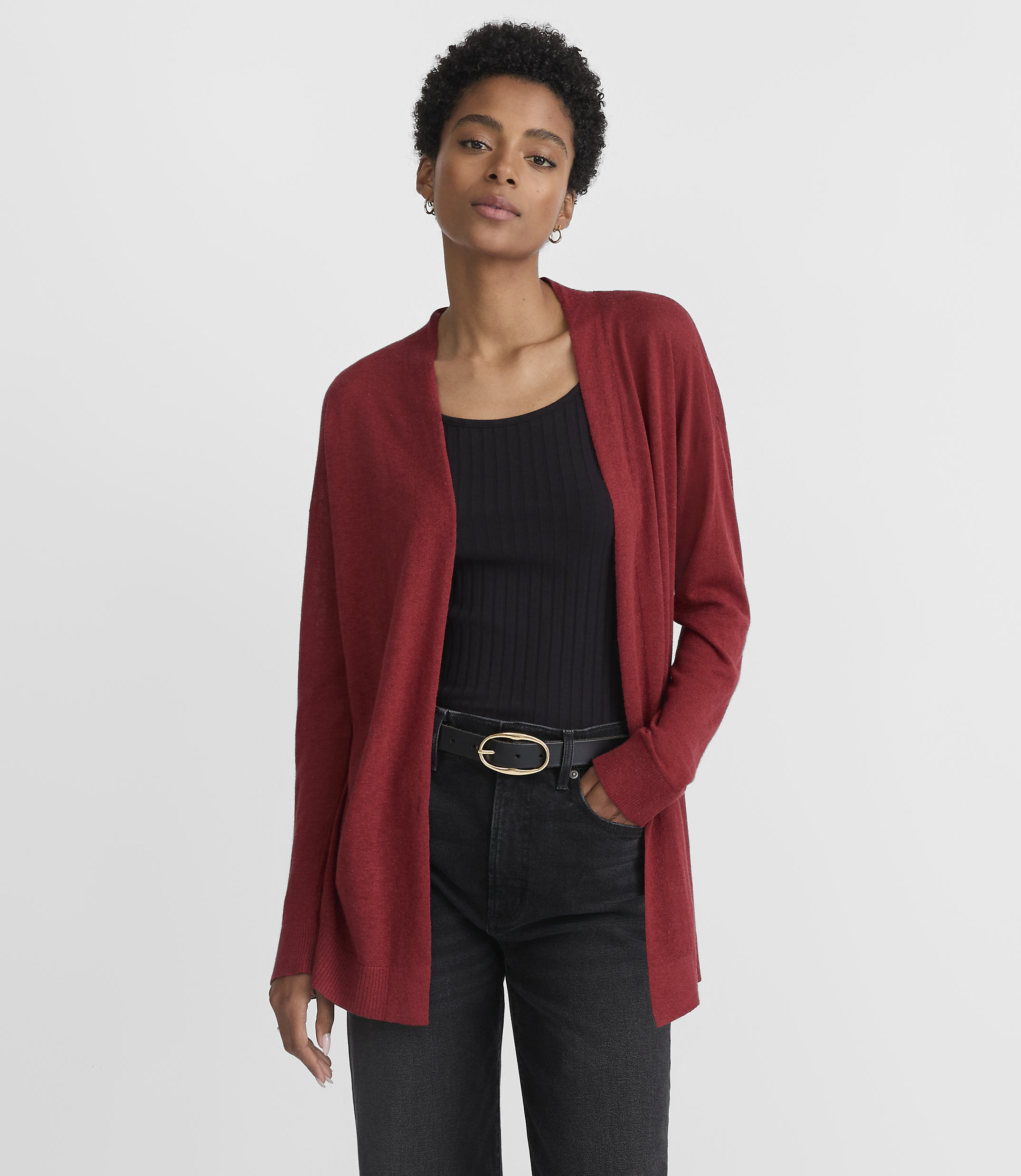 A woman in a red cardigan and black top stands against a plain gray background.