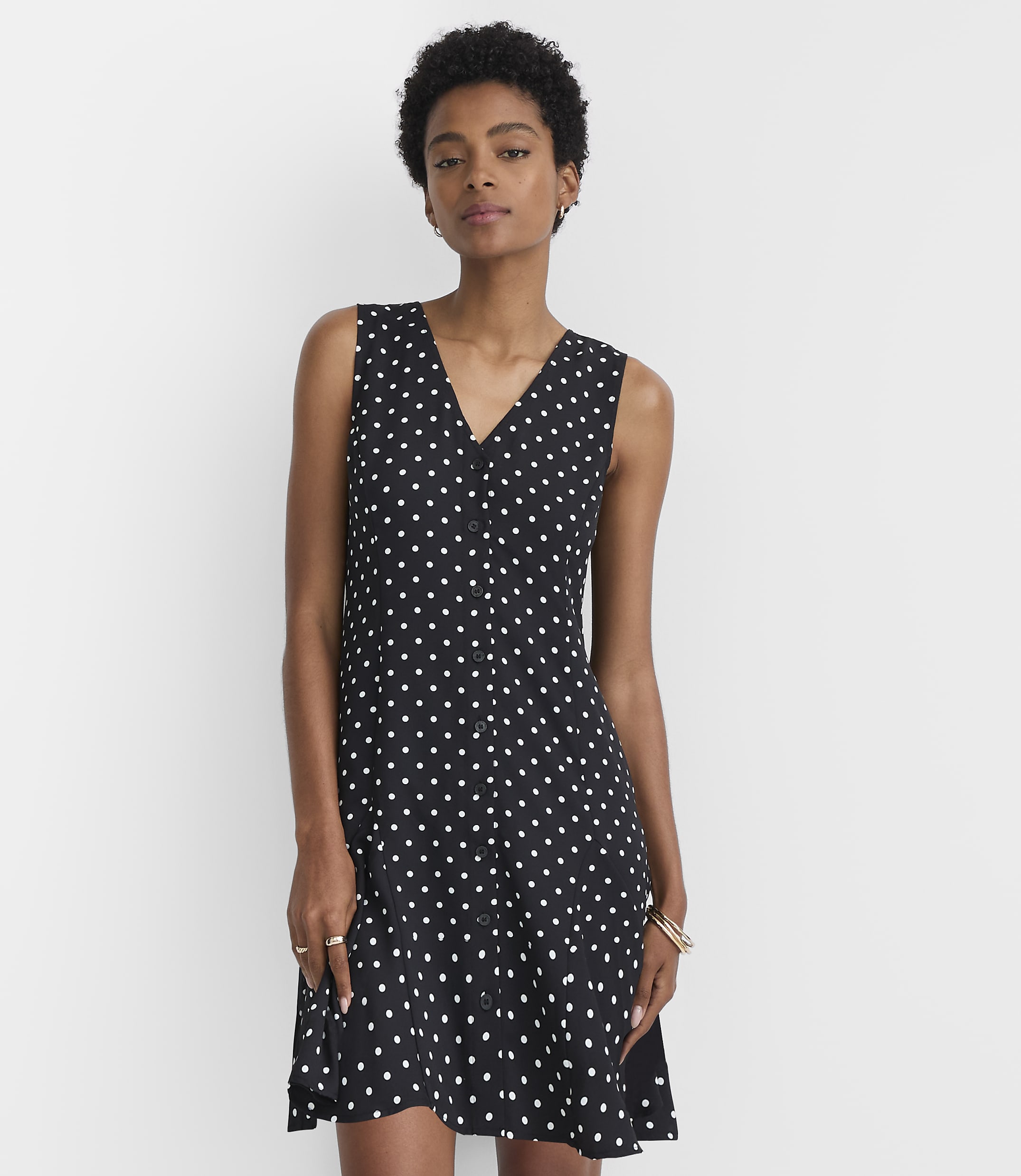 A woman in a black and white polka dot dress stands against a plain white background.