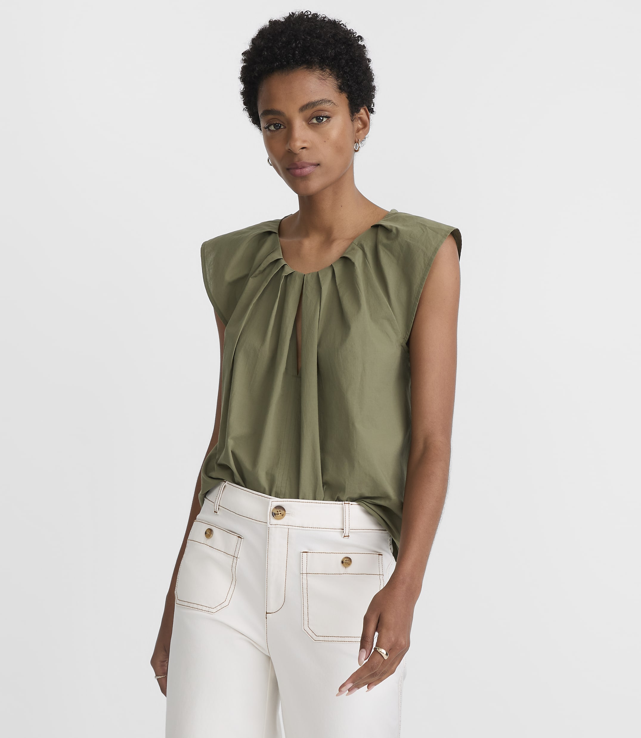 A woman in a green top and white pants stands against a plain white background.