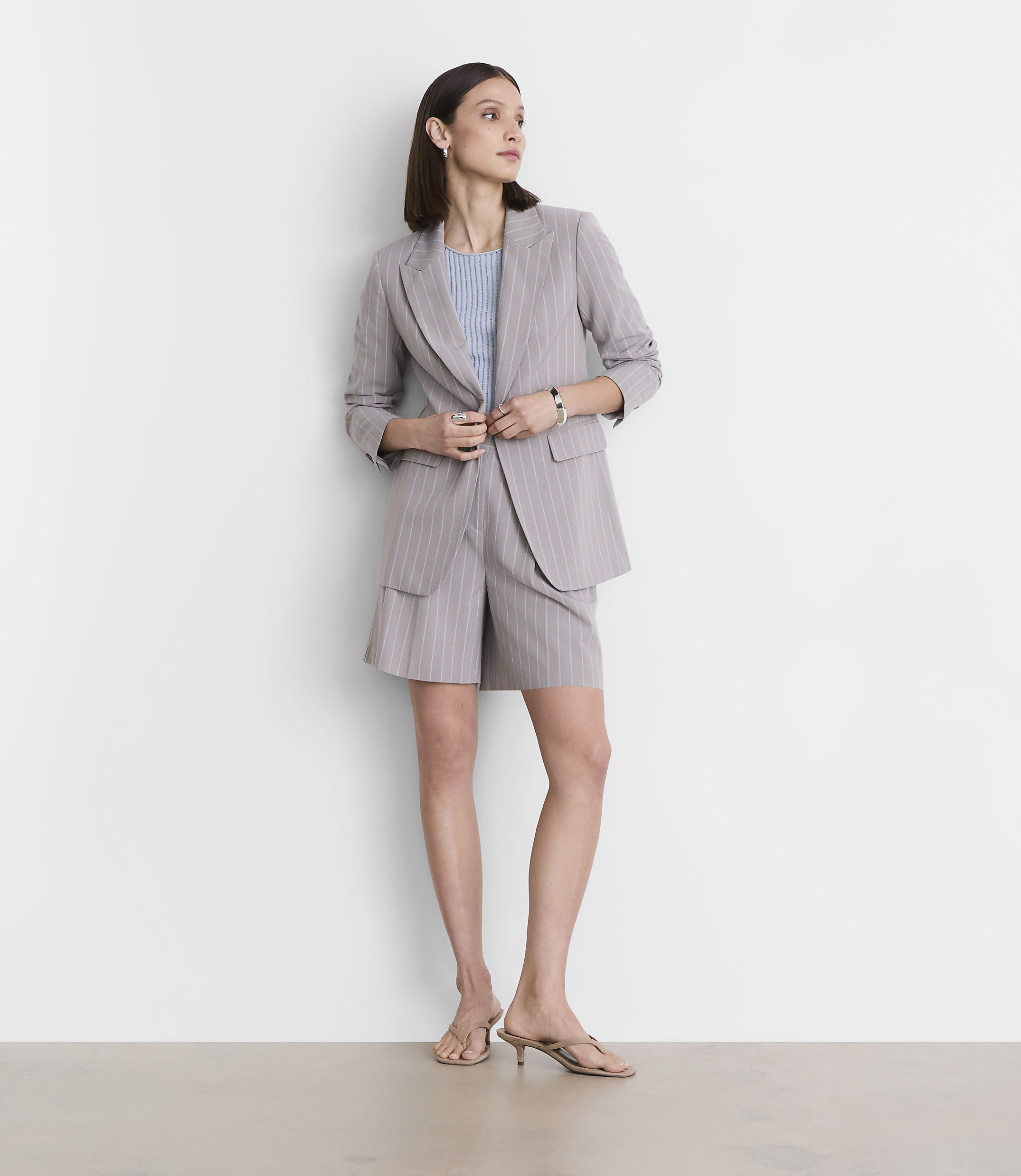 A woman in a pinstripe suit stands against a plain white wall.