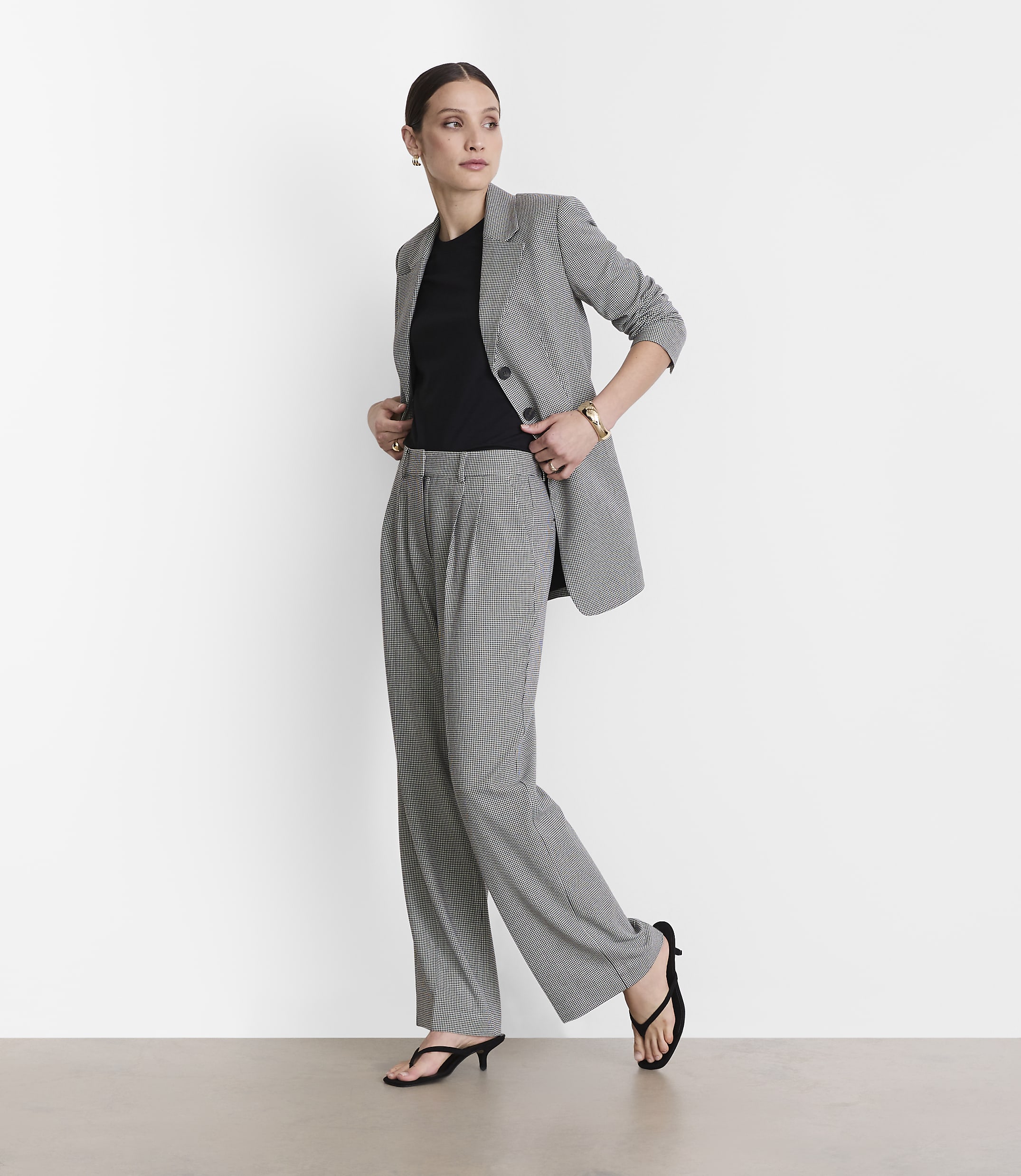 A woman in a black and white checkered suit stands against a plain white background.