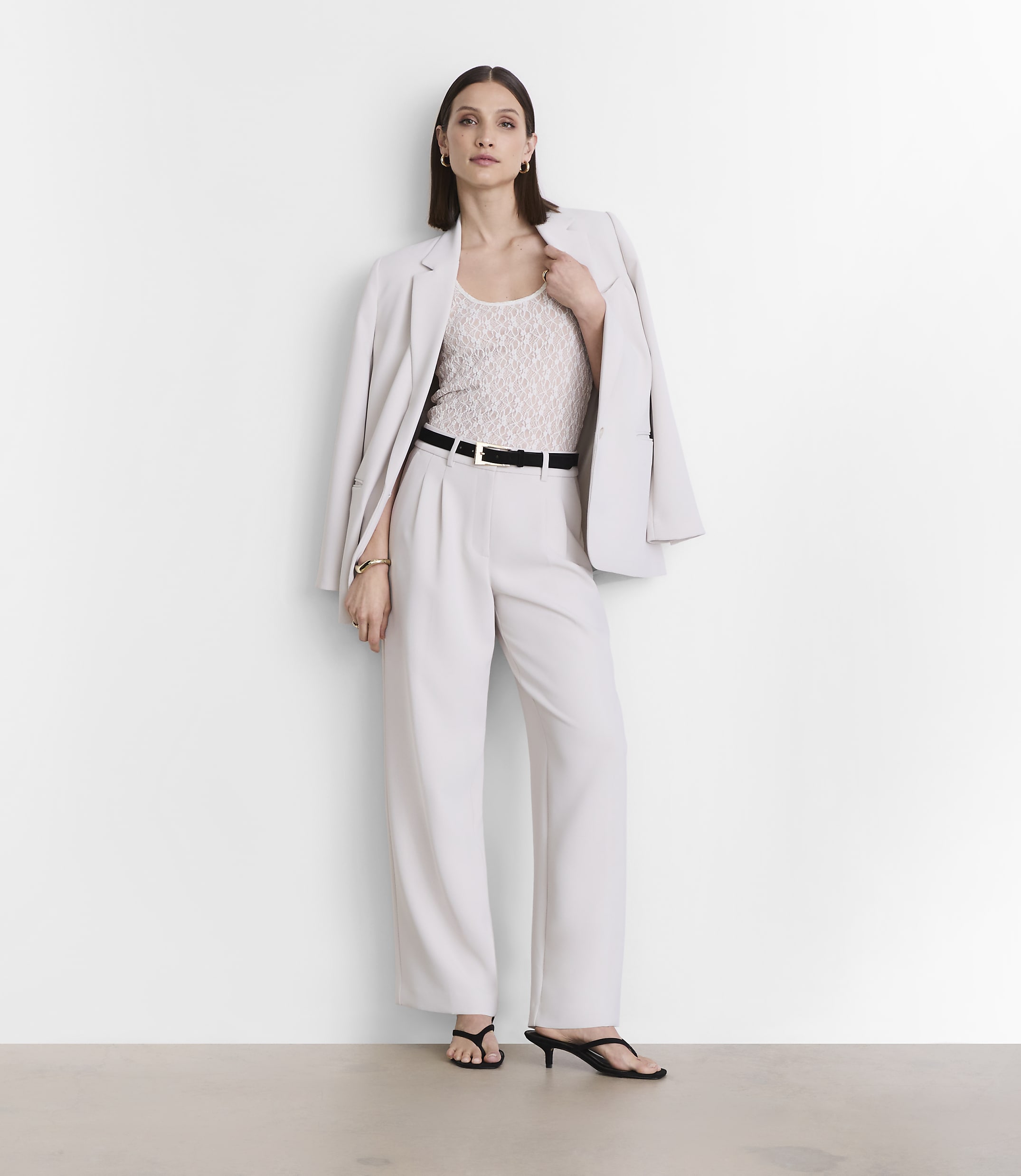 A woman in a light-colored suit stands against a plain white background.