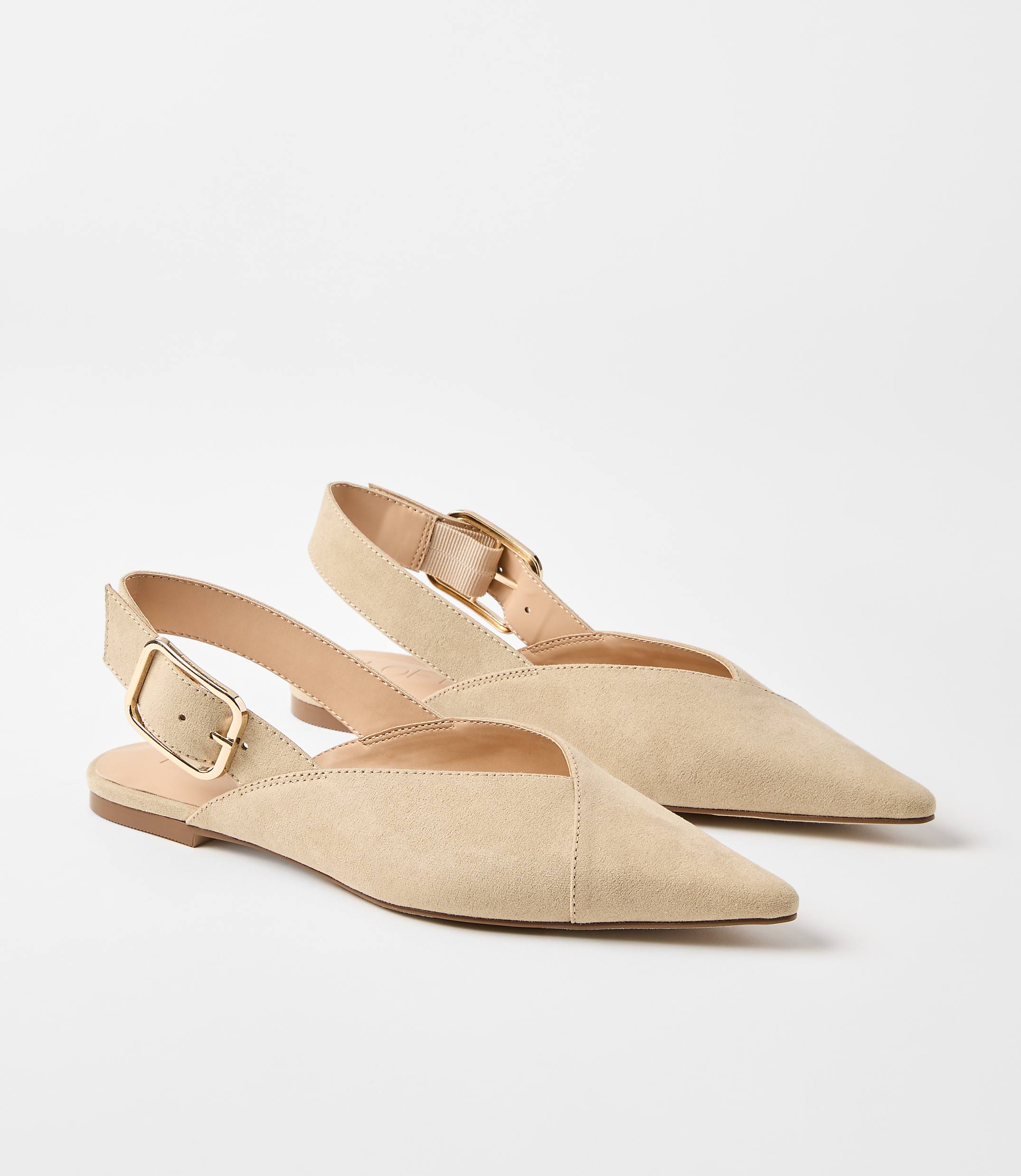 A pair of beige suede slingback flats with gold buckles rests on a plain white background.