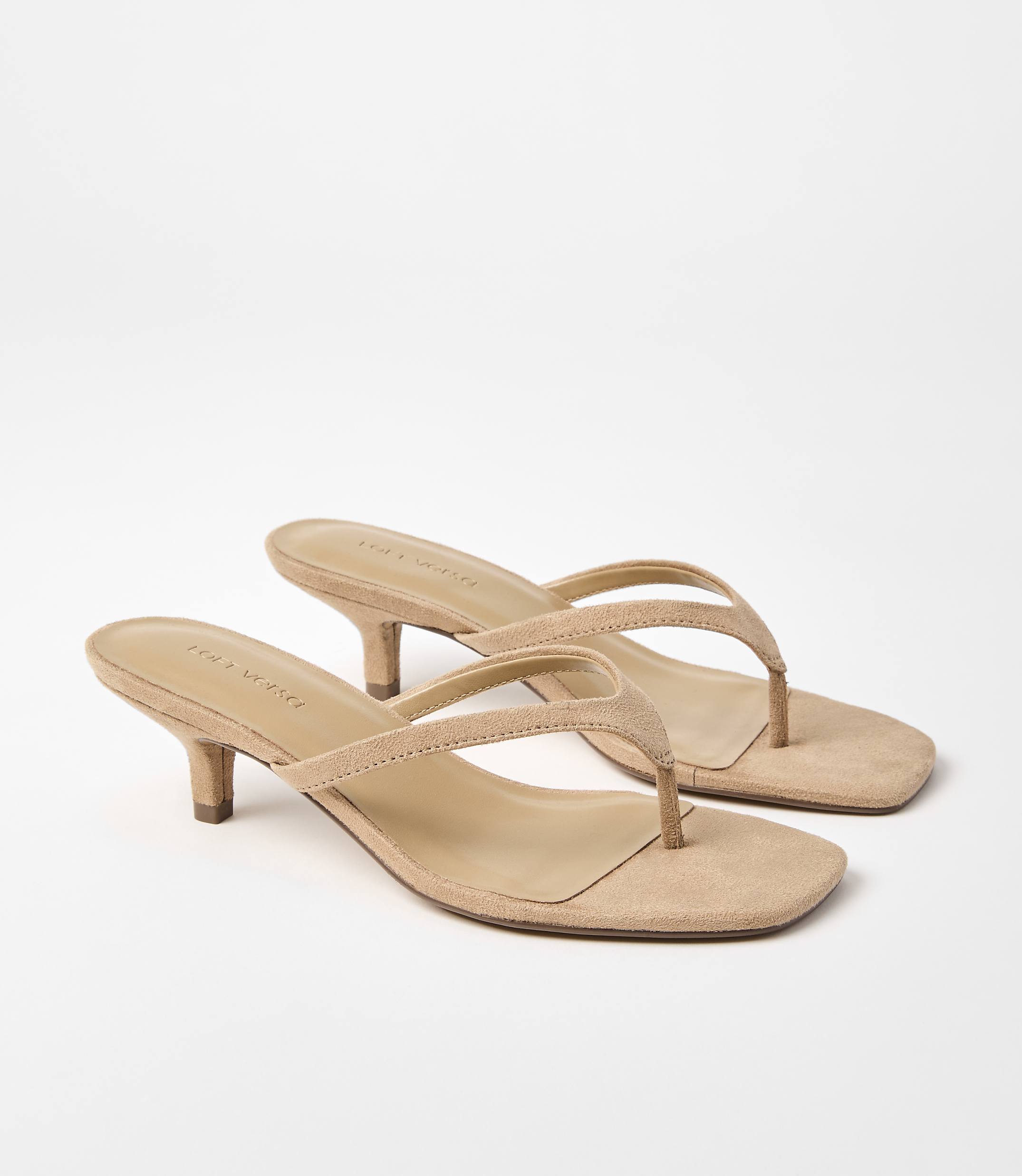 A pair of tan suede kitten heel thong sandals rests on a plain white background.