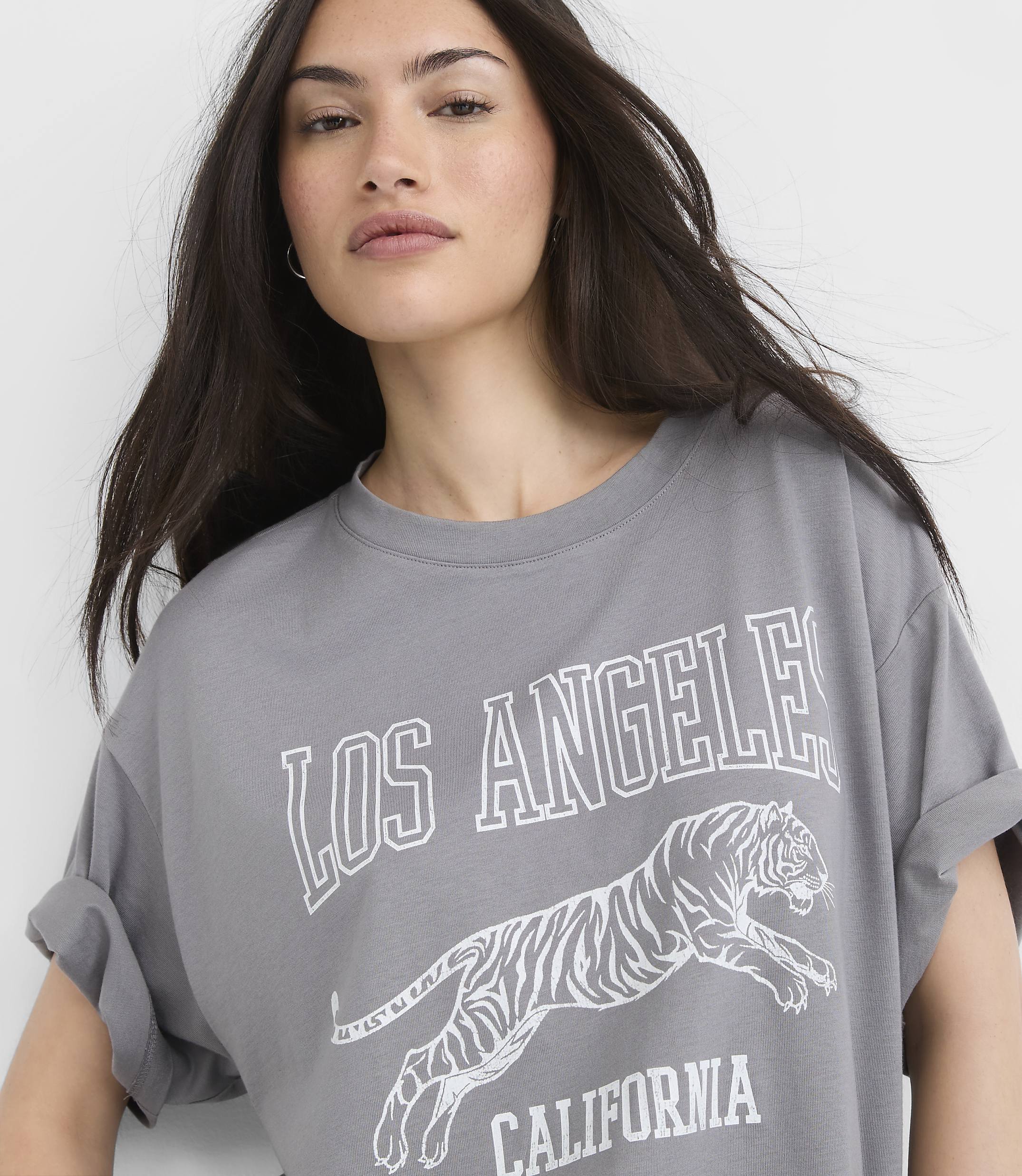 A woman in a grey t-shirt with a tiger graphic and "Los Angeles California" text stands against a plain white background.