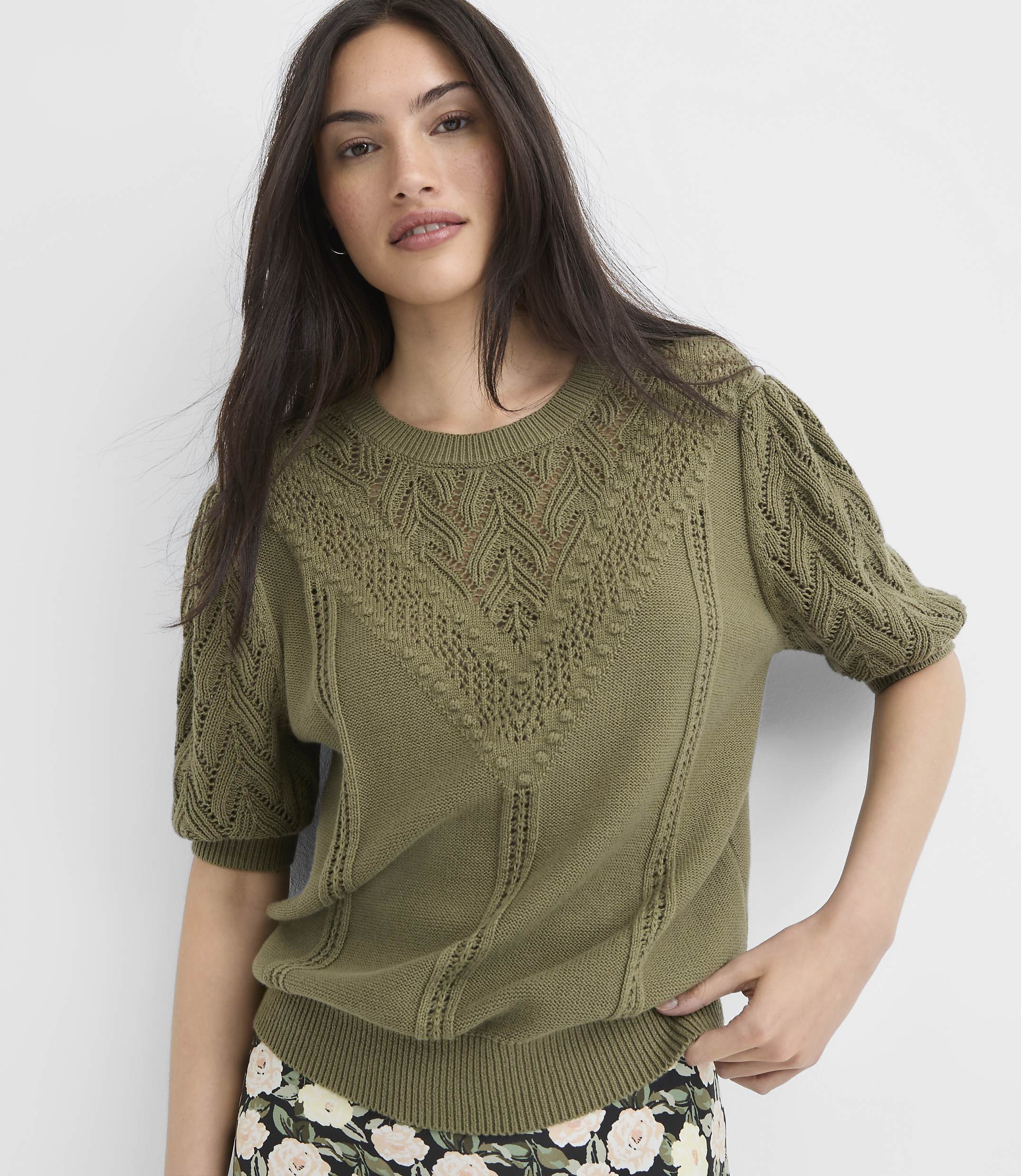A woman in a green, textured sweater stands against a plain white background.