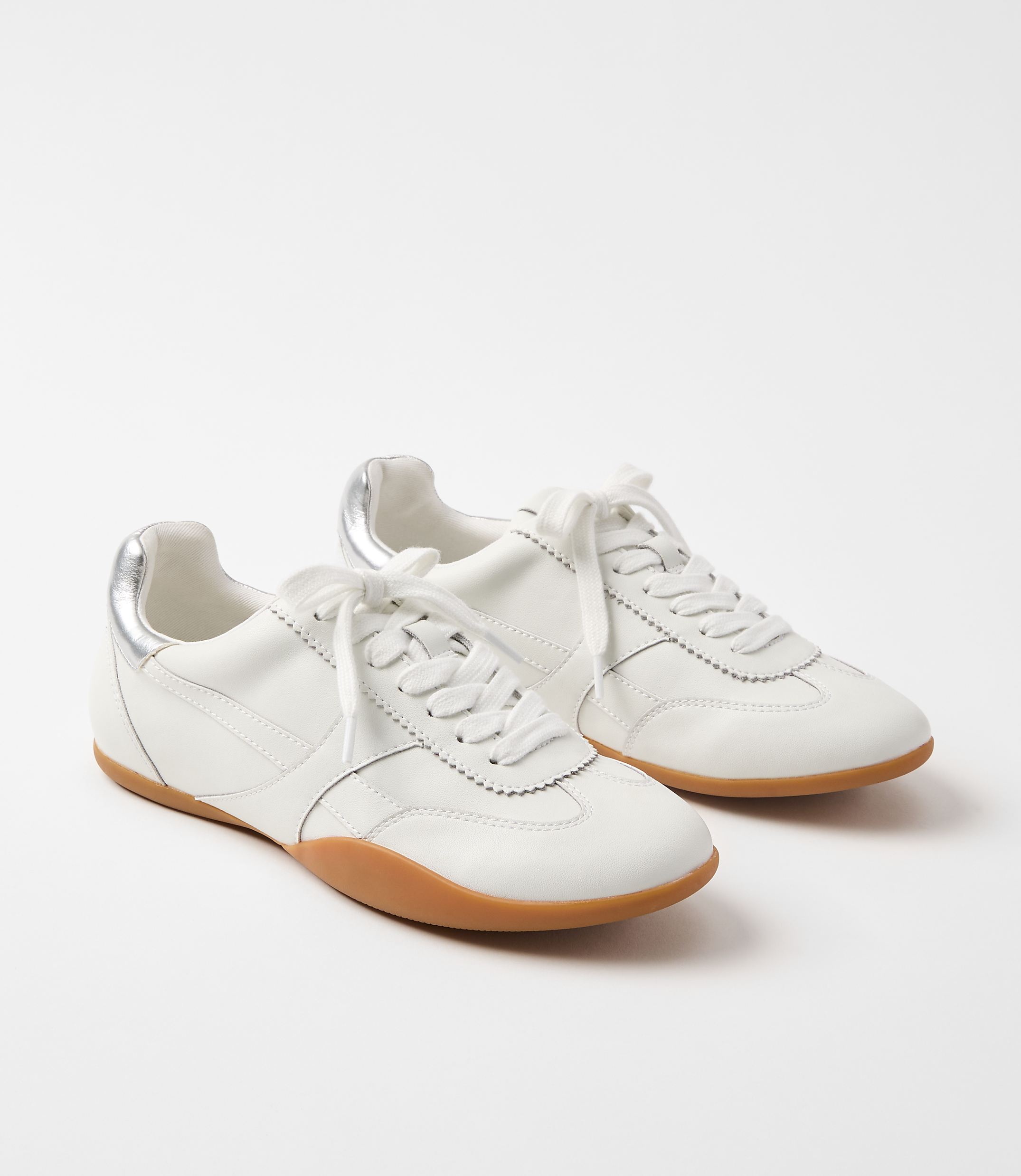 A pair of white leather sneakers with gum soles and silver accents rests on a plain white background.