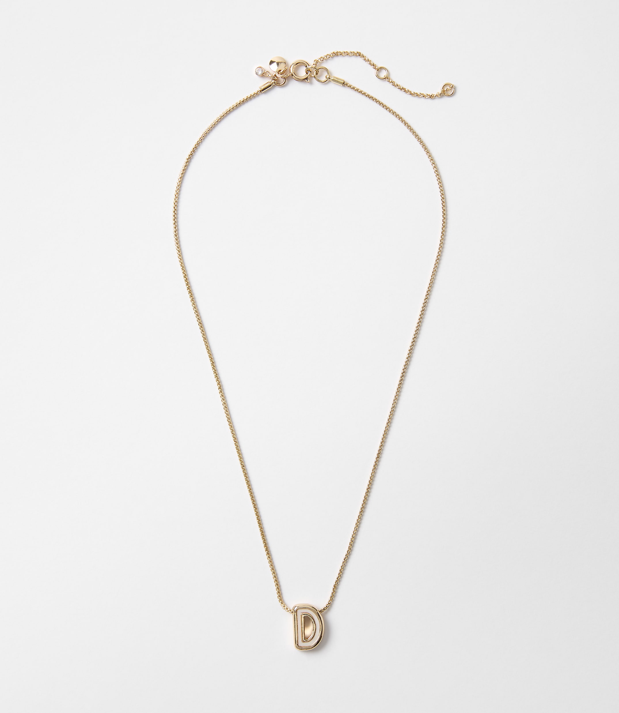 A delicate gold chain necklace with a stylized "D" pendant hangs against a plain white background.