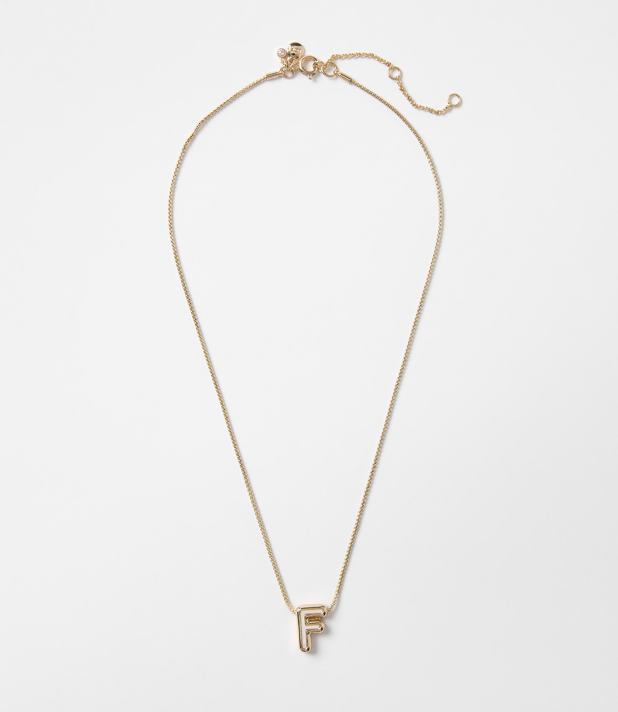 A delicate gold necklace with an "F" initial pendant hangs against a plain white background.