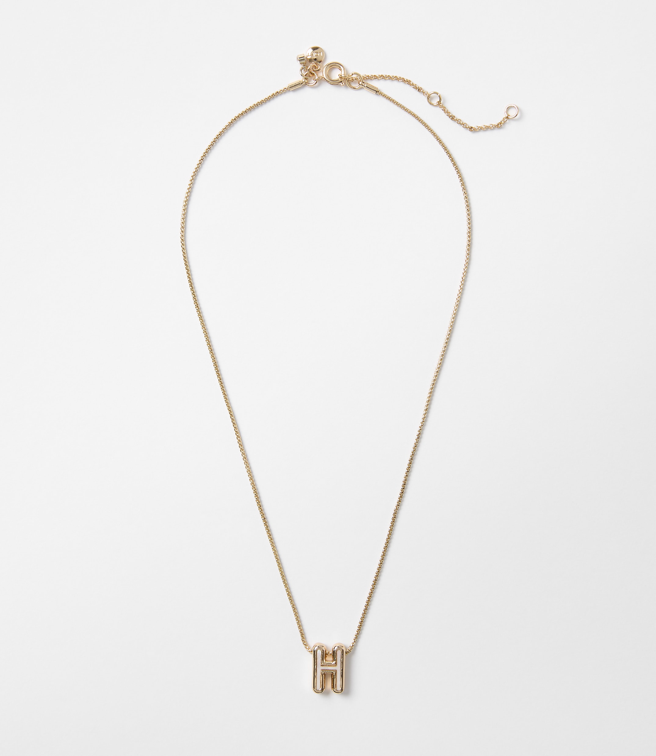 A delicate gold chain necklace with a block letter "H" pendant hangs against a plain white background.