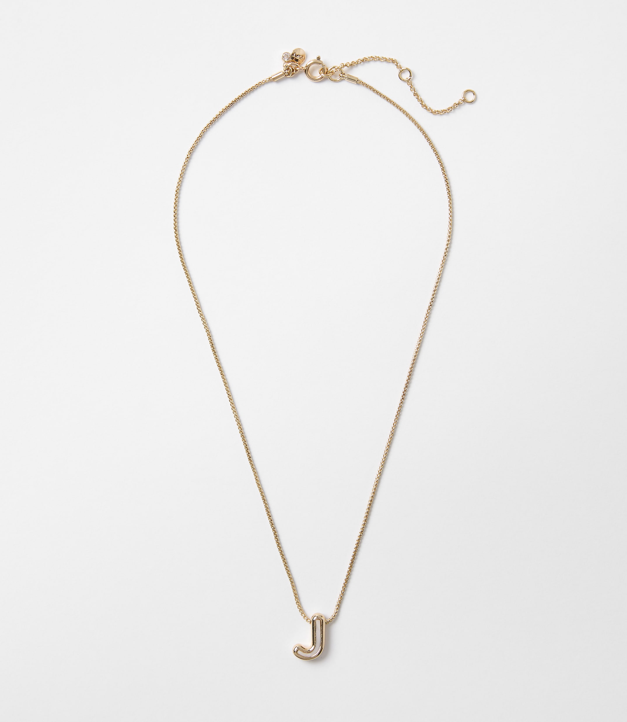 A delicate gold necklace with a stylized "J" pendant hangs against a plain white background.