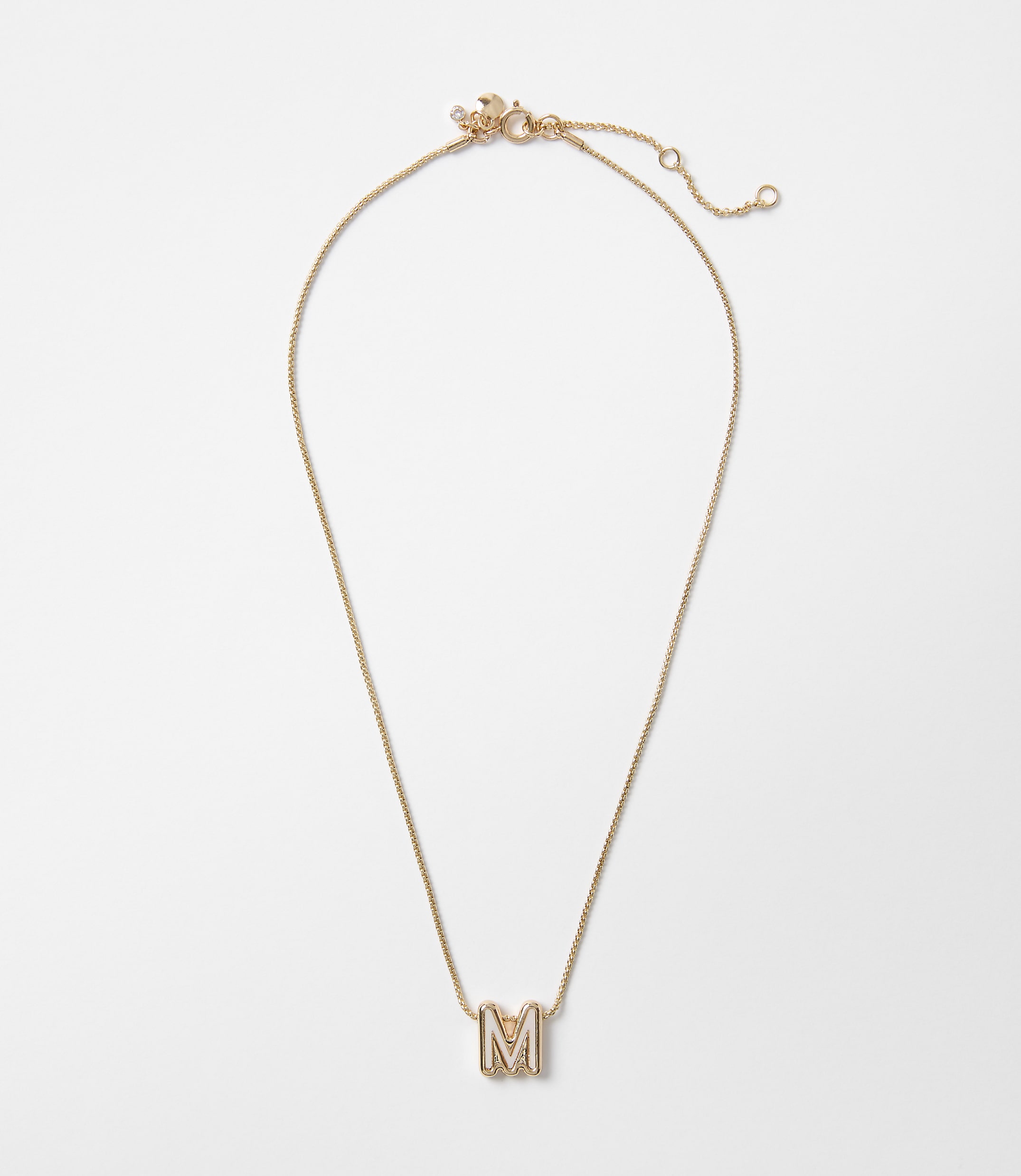 A delicate gold necklace with an "M" pendant rests on a plain white background.
