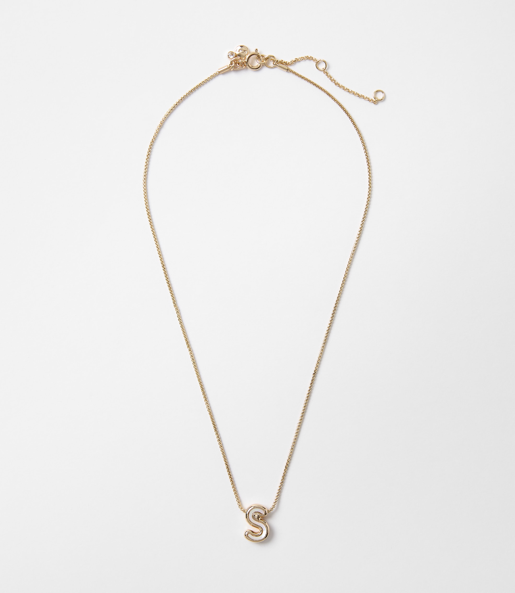 A delicate gold necklace with a sparkling letter "S" pendant hangs against a plain white background.
