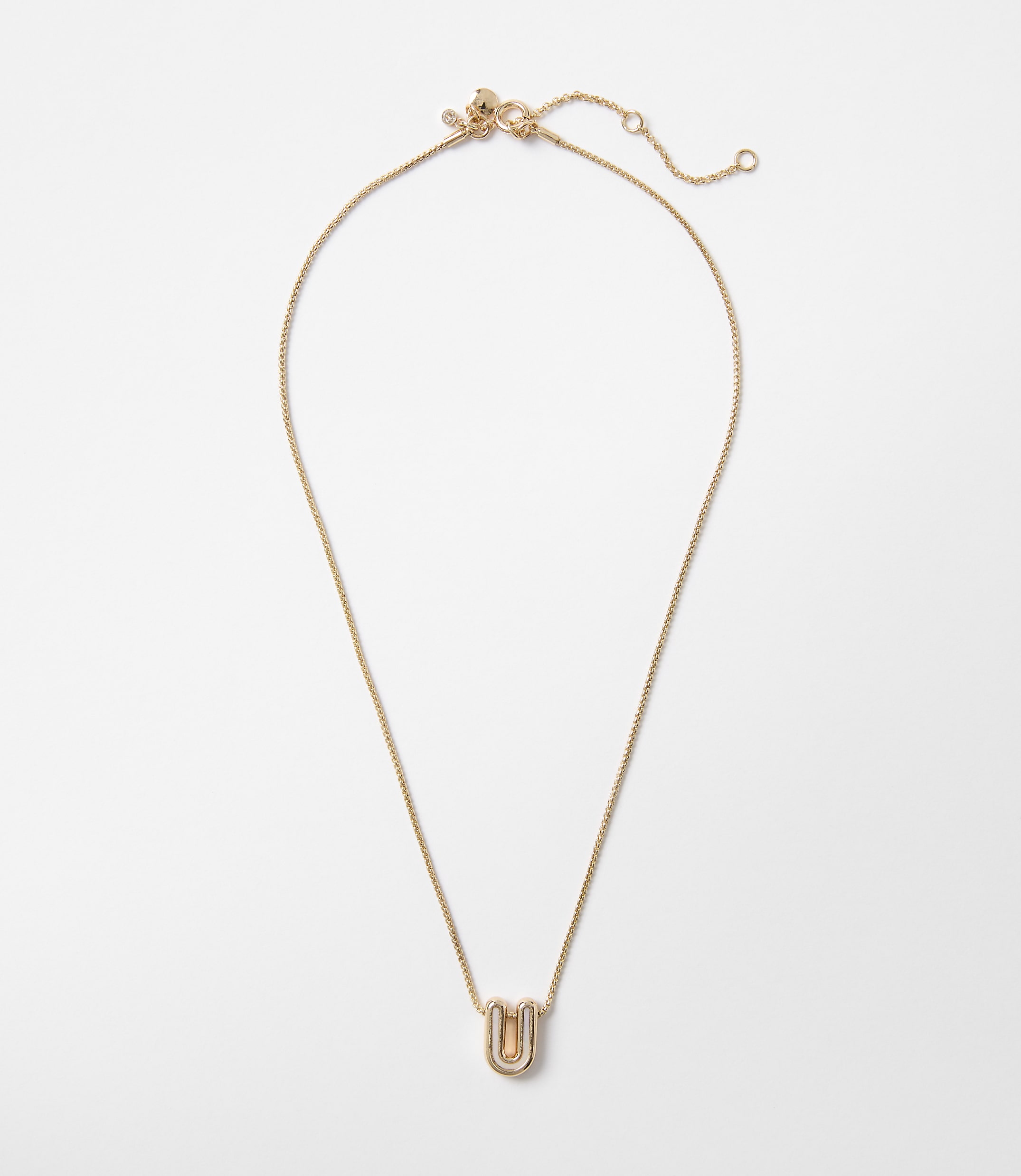 A delicate gold necklace with a stylized "U" pendant rests on a plain white background.