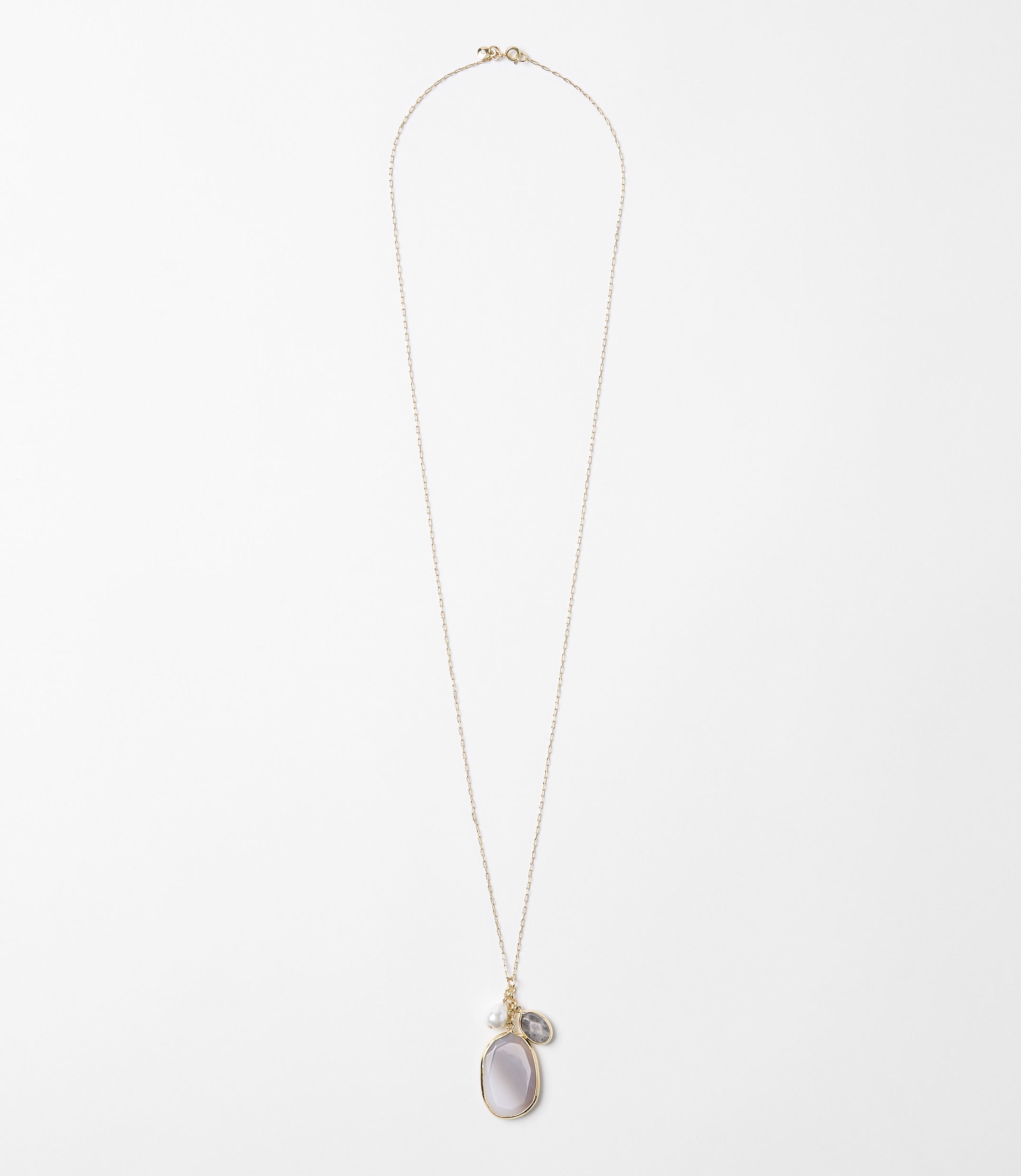 A delicate rose gold chain necklace with a pearlescent oval pendant and a small grey stone hangs against a plain white background.