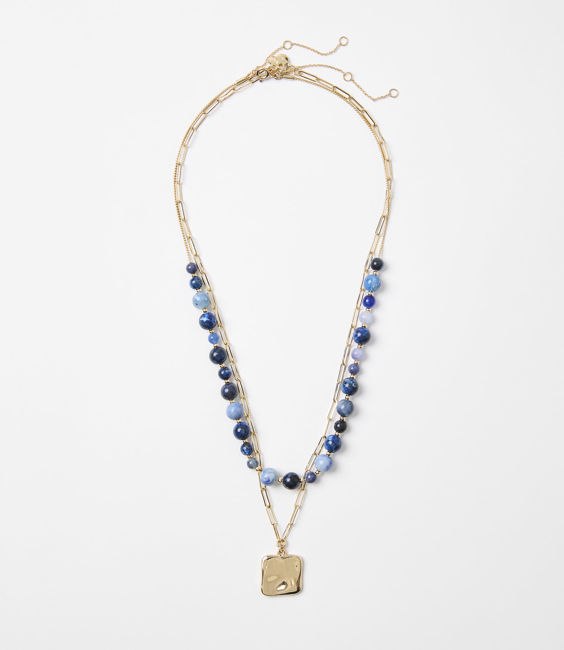 A delicate gold necklace with blue beads and a square pendant rests on a plain white background.