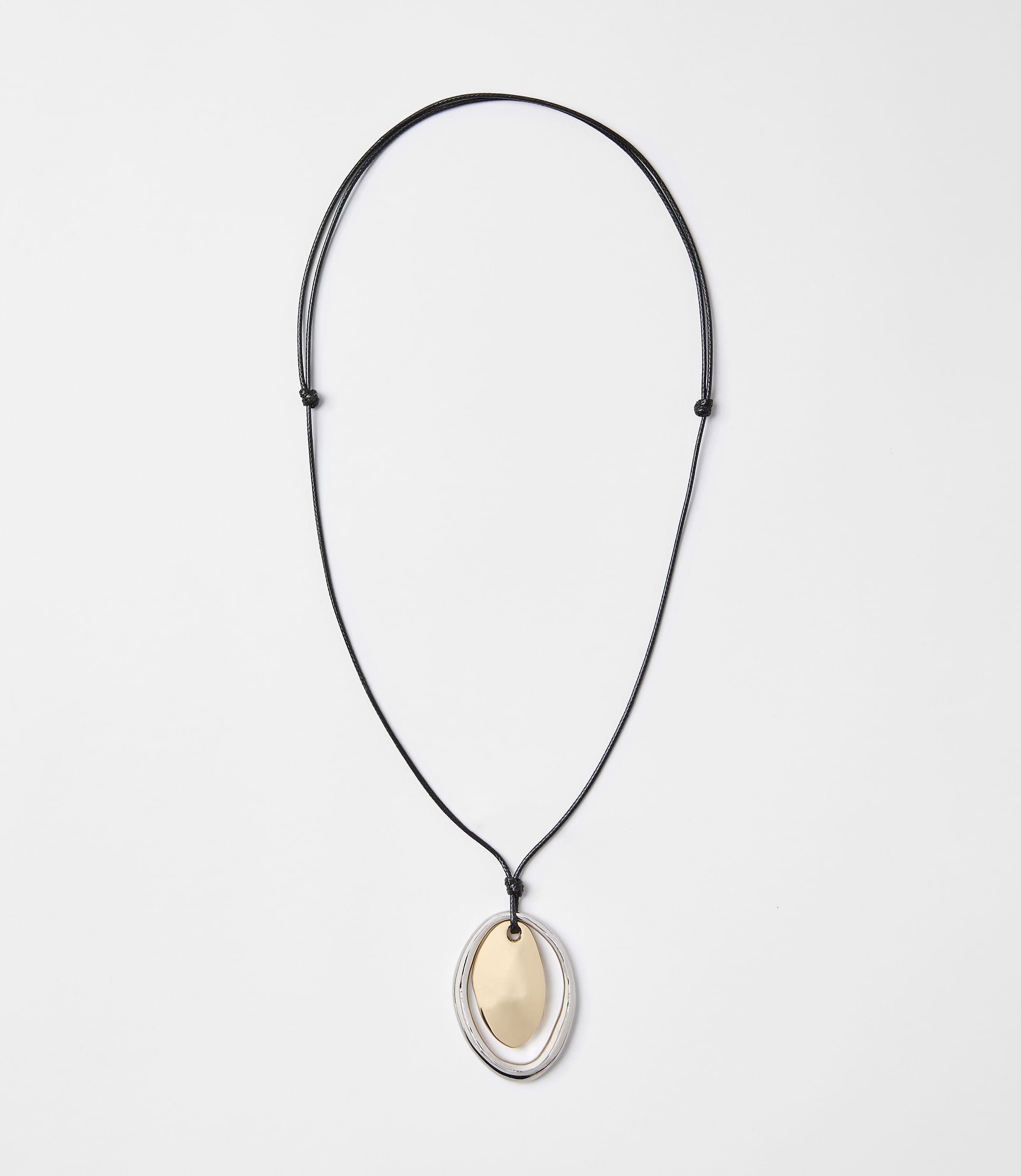 A black cord necklace with a layered oval pendant of gold and silver hangs against a plain white background.