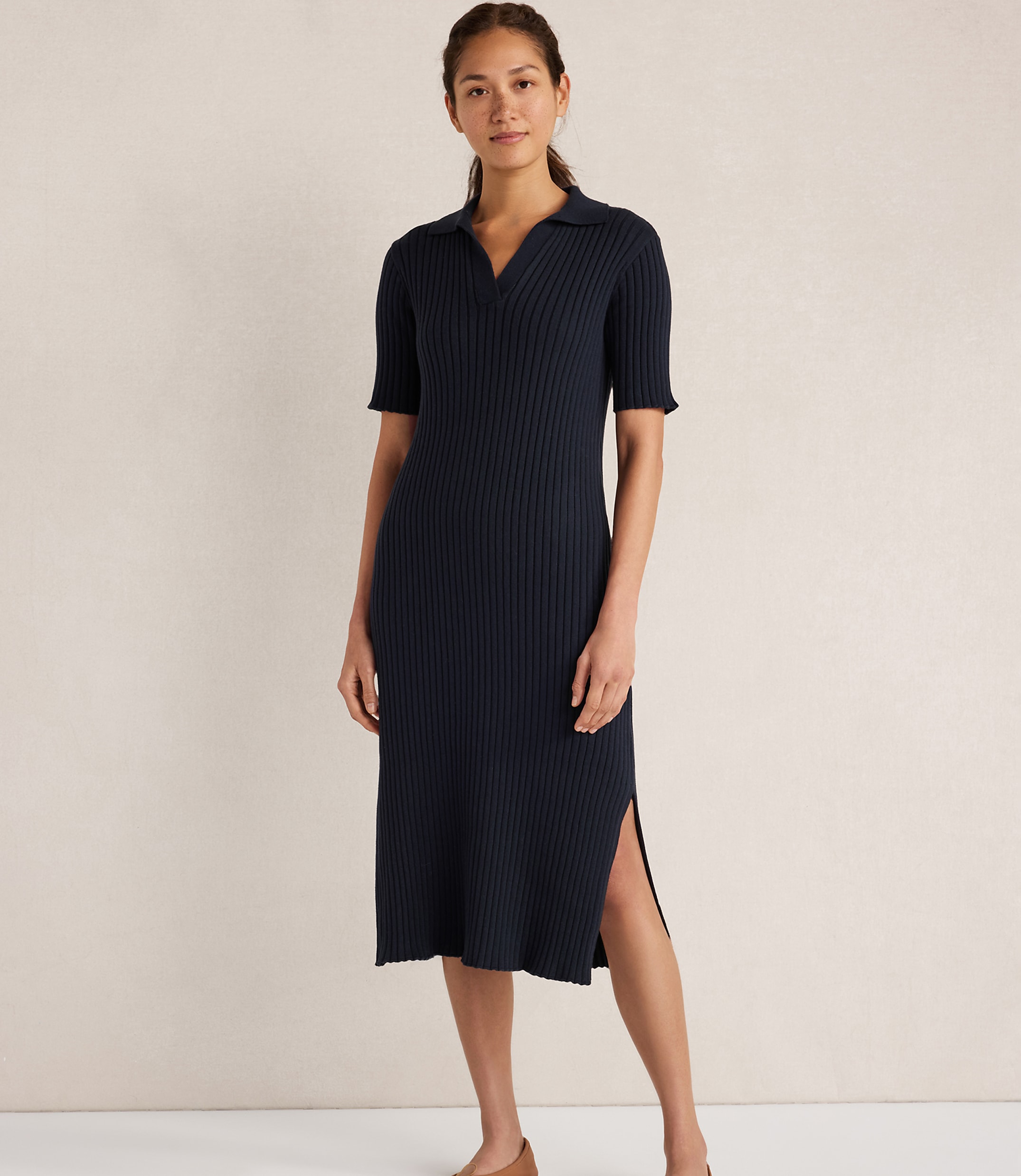A woman in a navy blue ribbed knit polo dress stands against a plain, light-colored background.