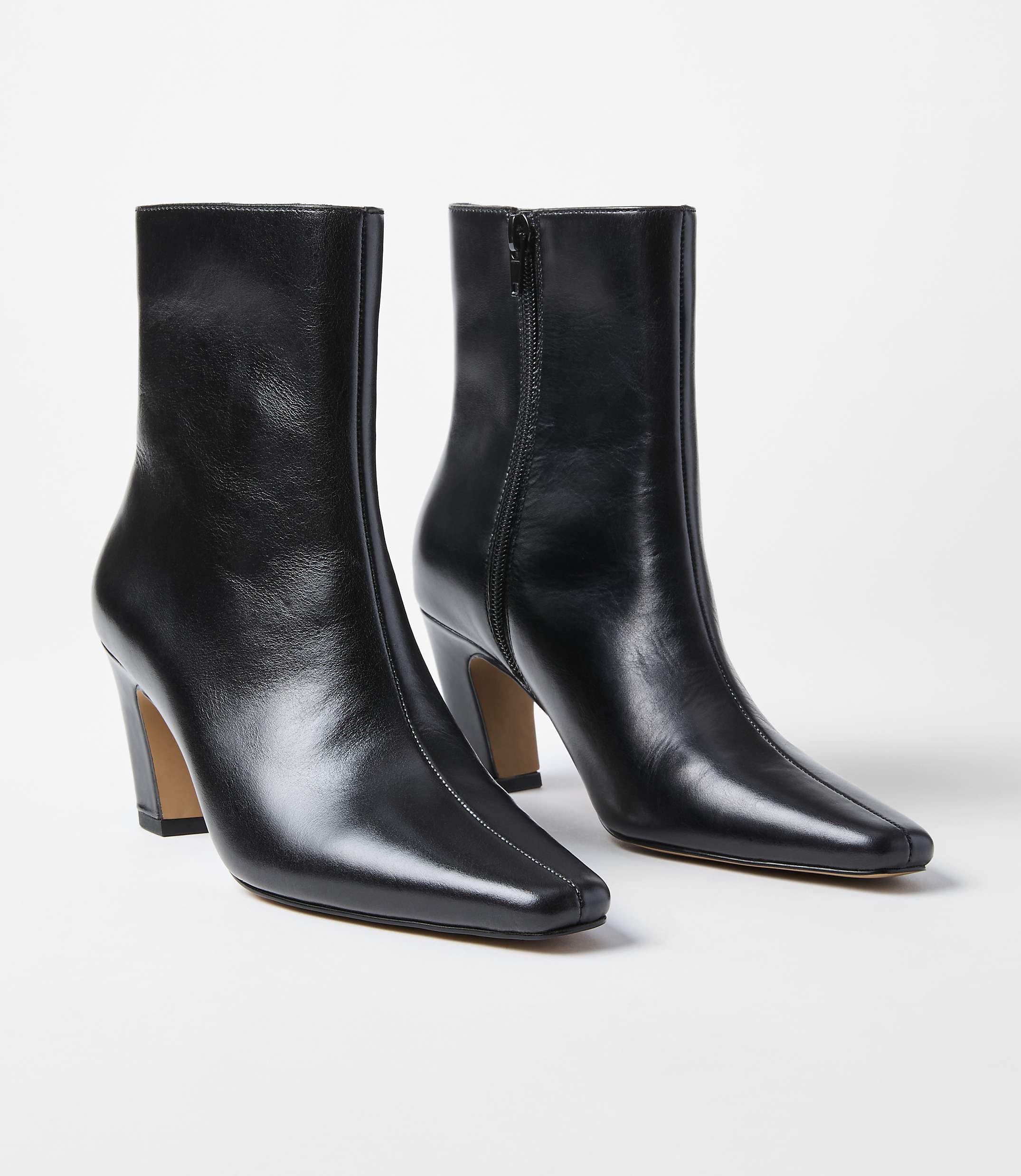 A pair of black leather ankle boots with square toes and block heels stand on a white background.