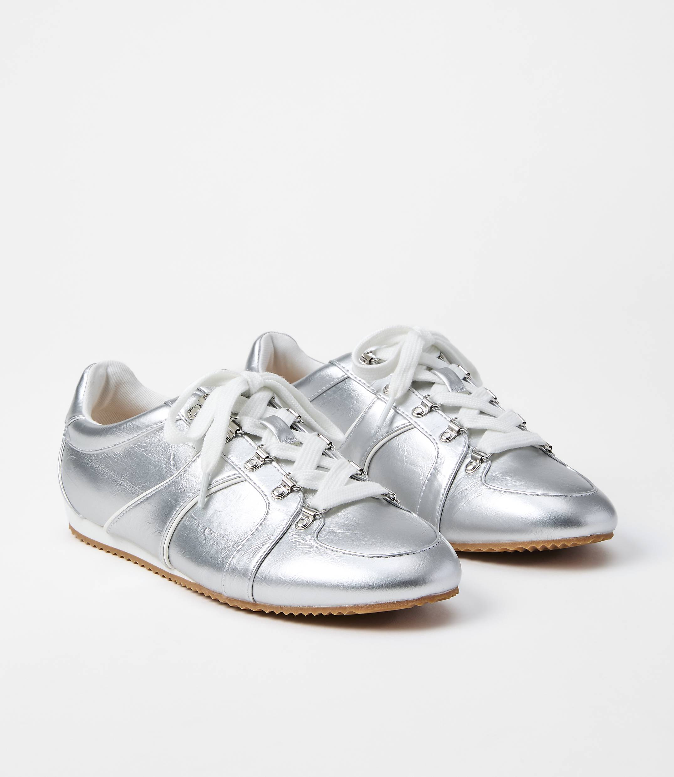 A pair of shiny silver sneakers with white laces rests on a plain white background.