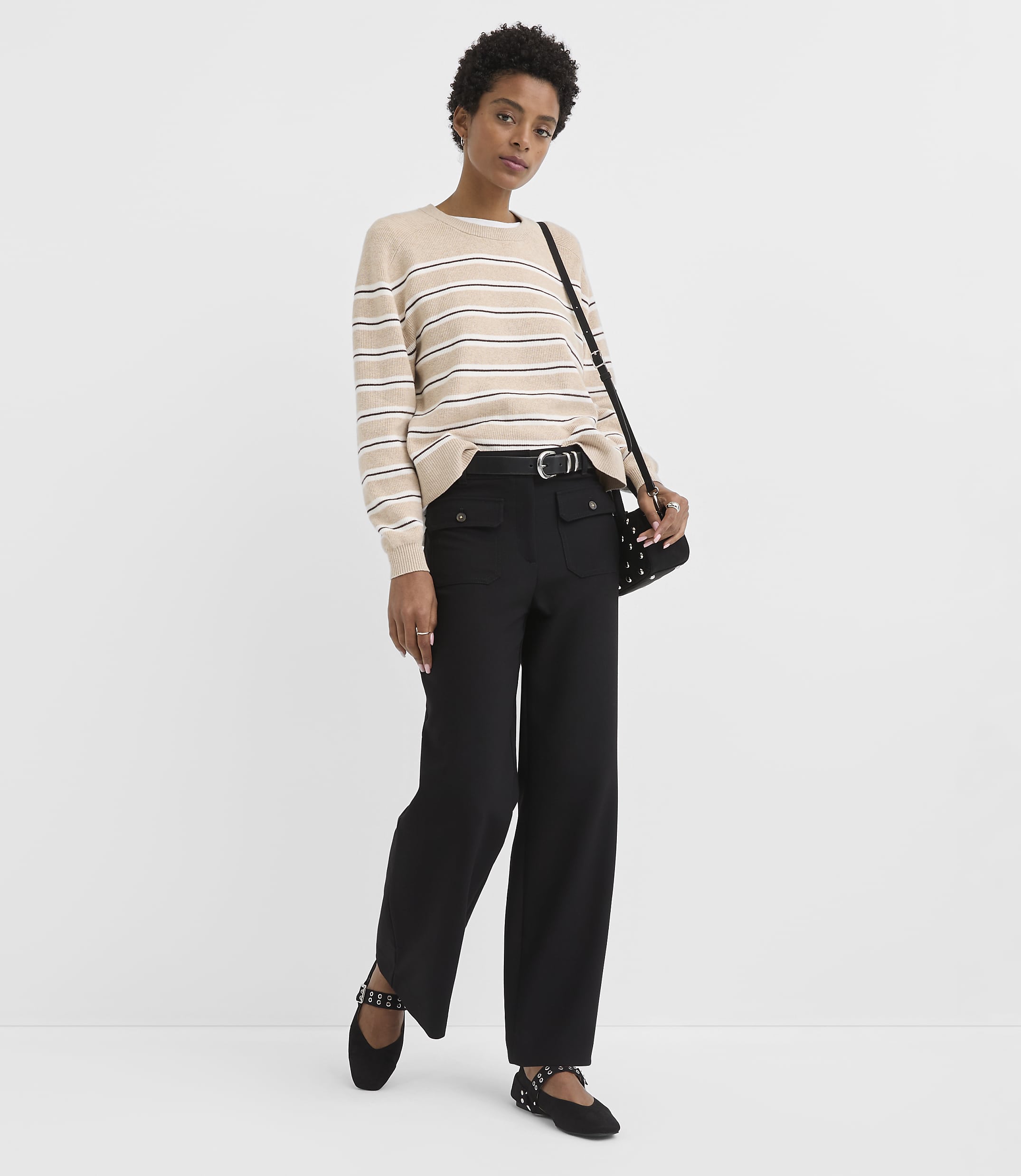 A woman in a striped sweater and black pants stands against a plain white background.