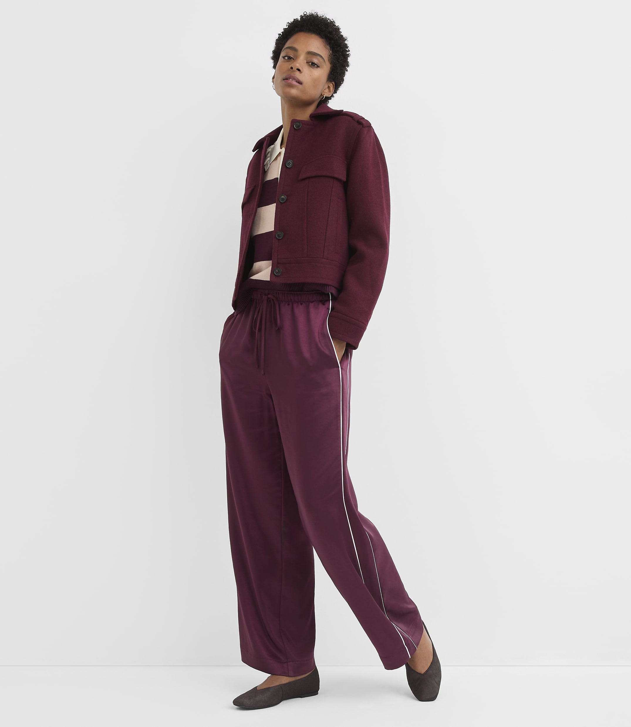 A woman in a burgundy jacket and matching pants stands against a plain white background.