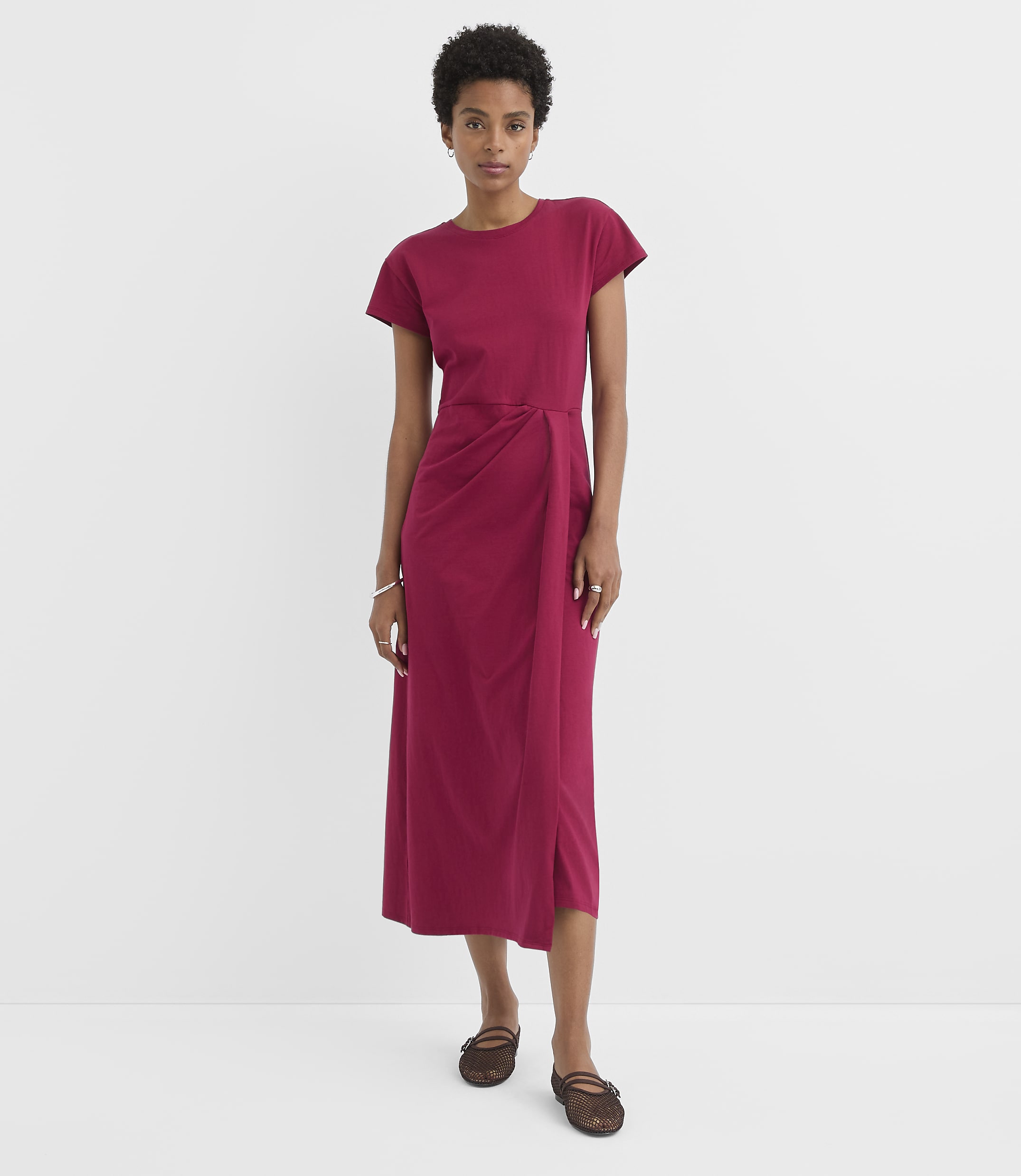 A woman in a magenta dress stands against a plain white background.