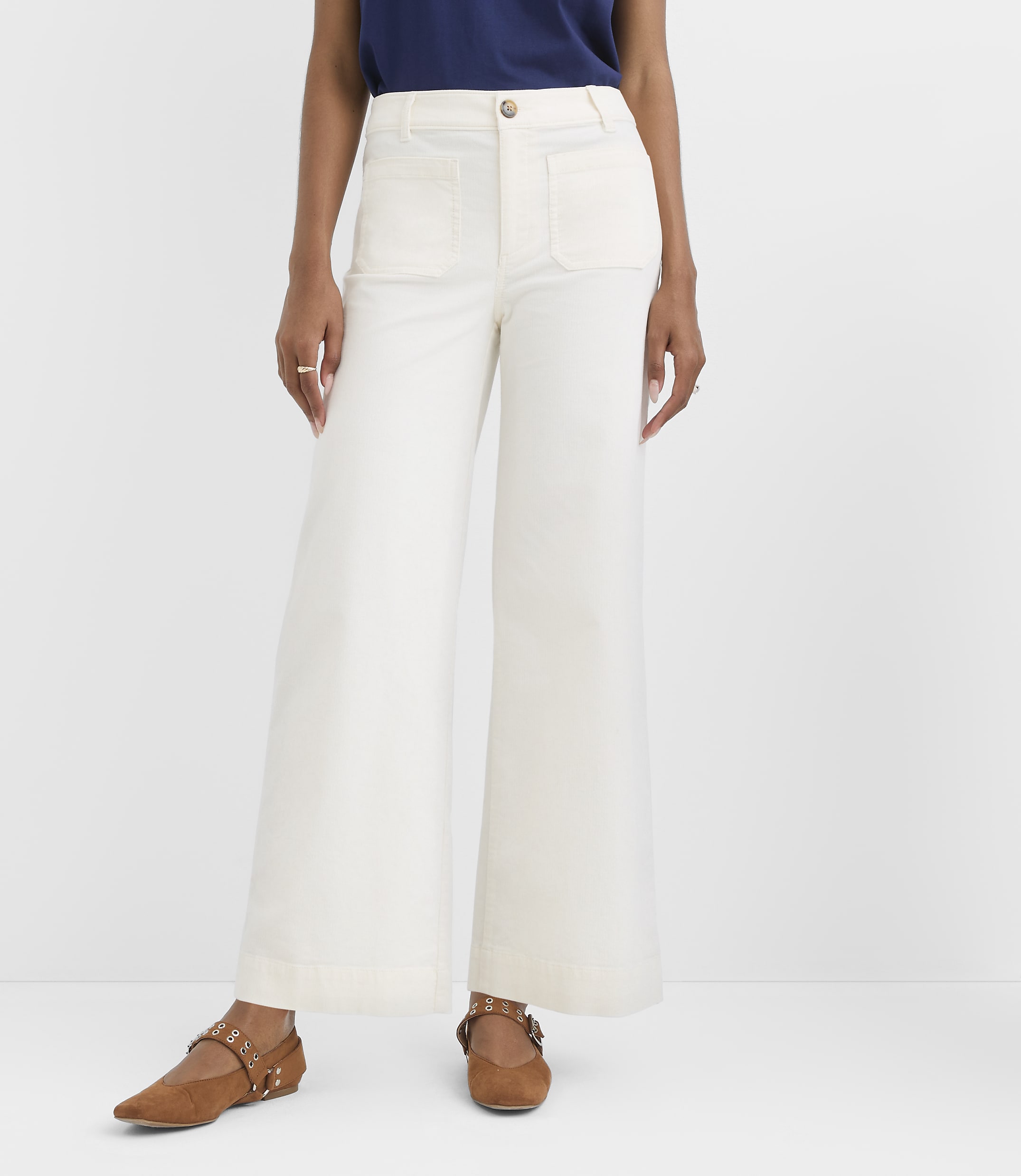 A person wearing white wide-leg pants and brown flats stands against a plain white background.